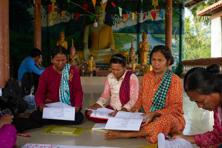 A group of people sitting in a circle holding papers speaking to each other