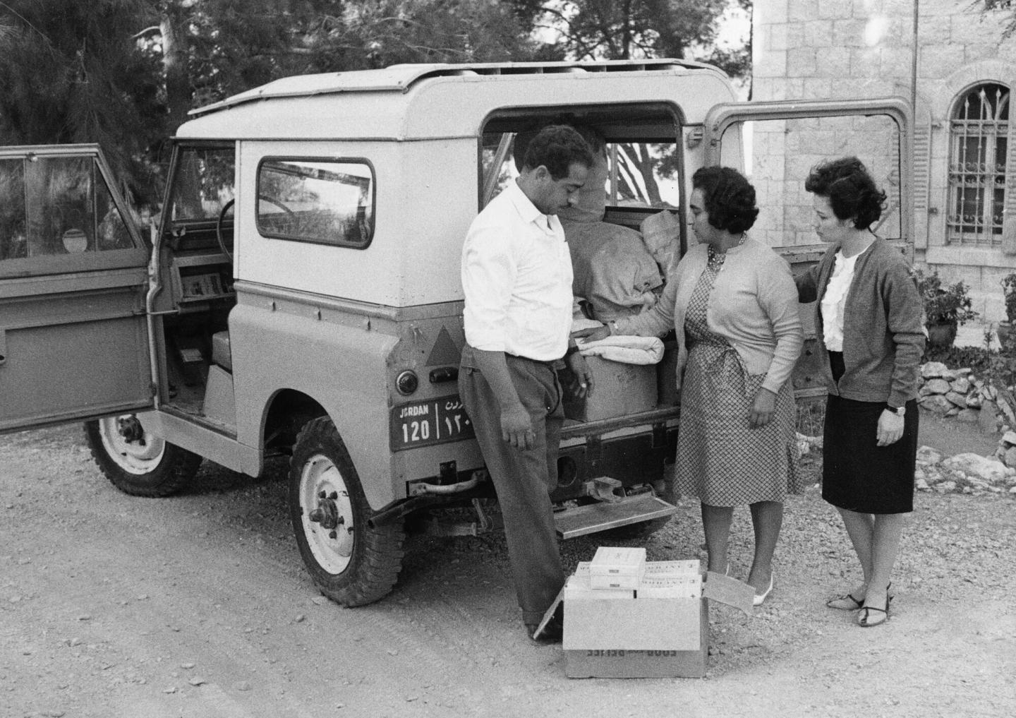 A black and white photo of two women and a man unloading supplies from a vehicle