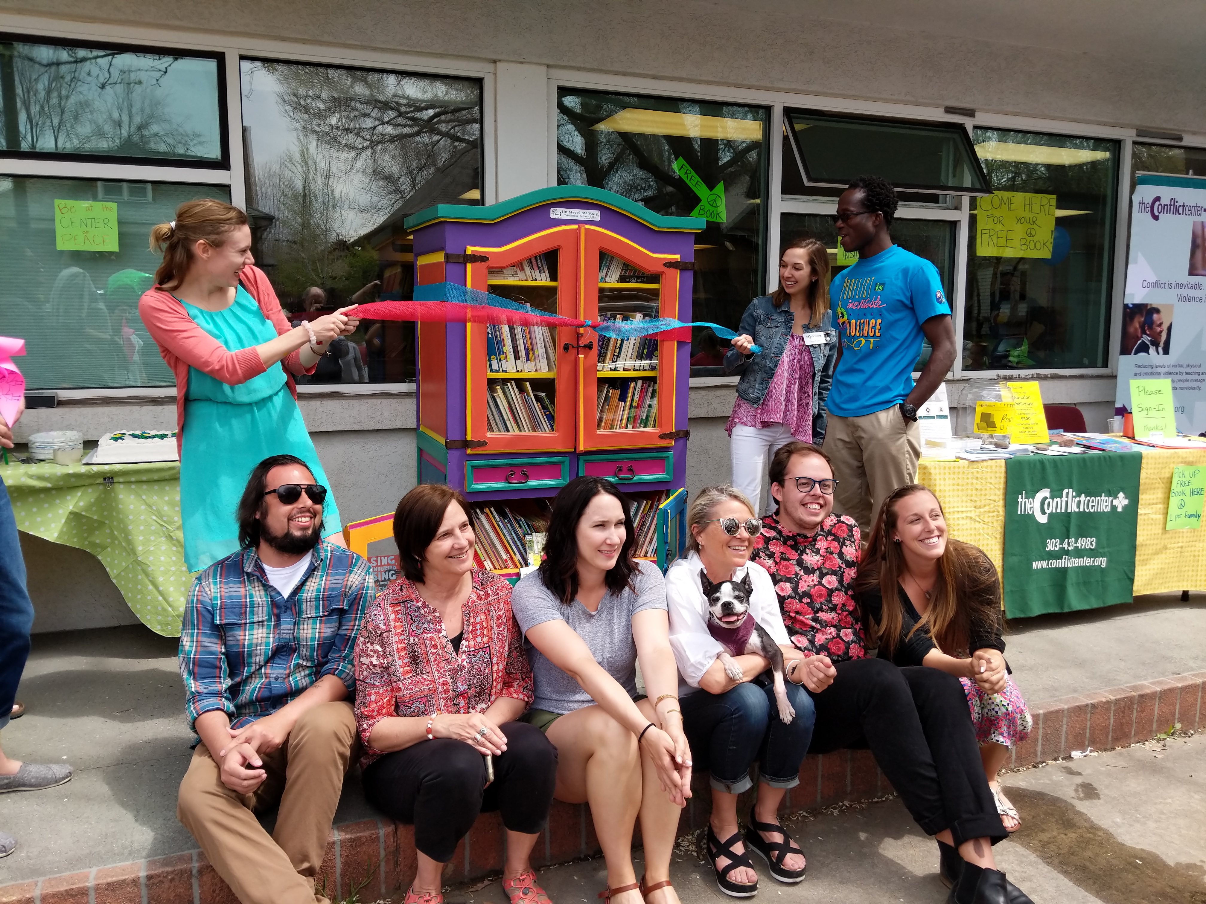 A group of young adults sit on a curb outside a building.