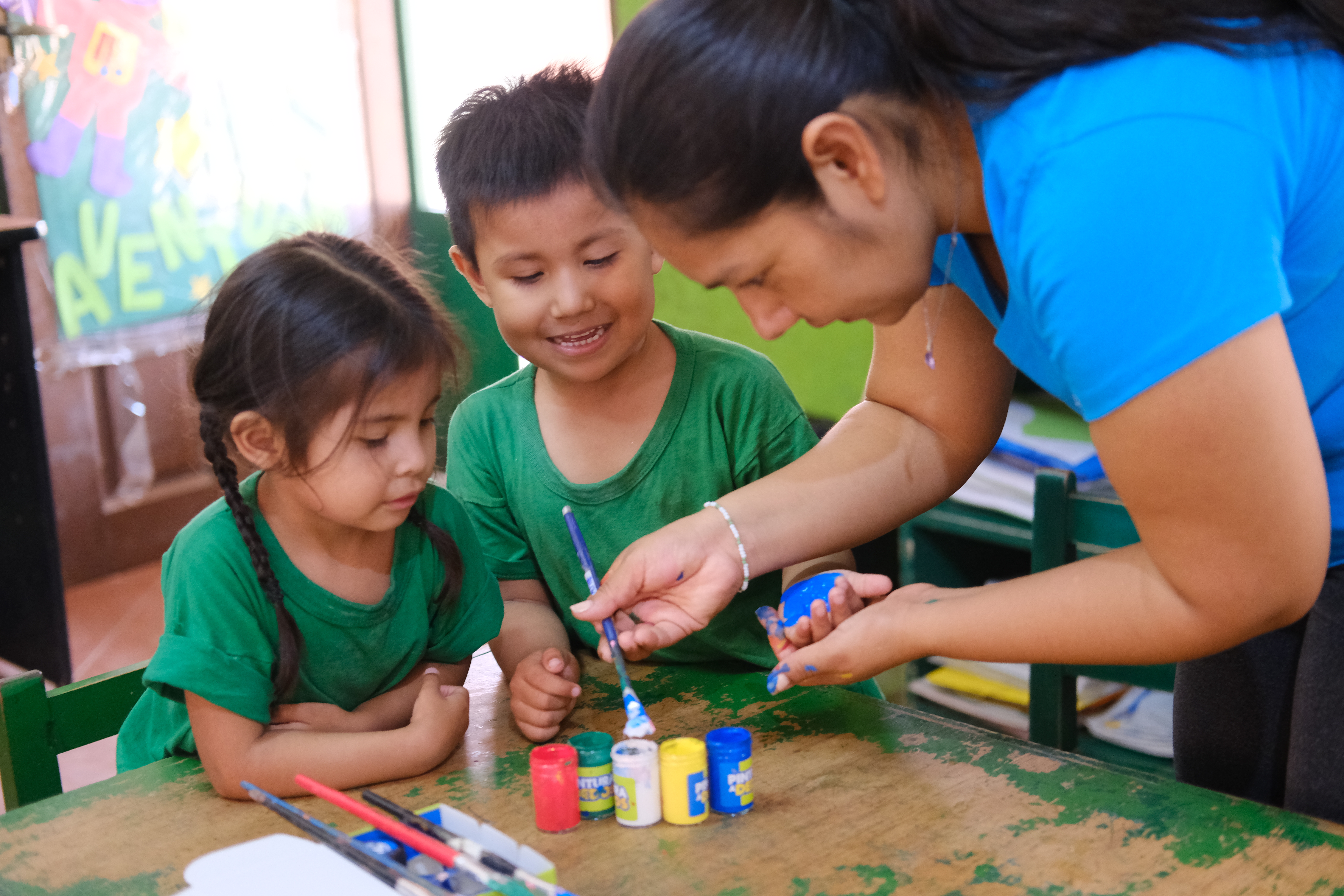 Four-year-olds Isabella Villarroel Muñoz (left) and Caleb Poichee Lima have their hands painted by Claudia Patricia Meruvia Céspedes, an educator at Samuelito Daycare, as part of an art activity.