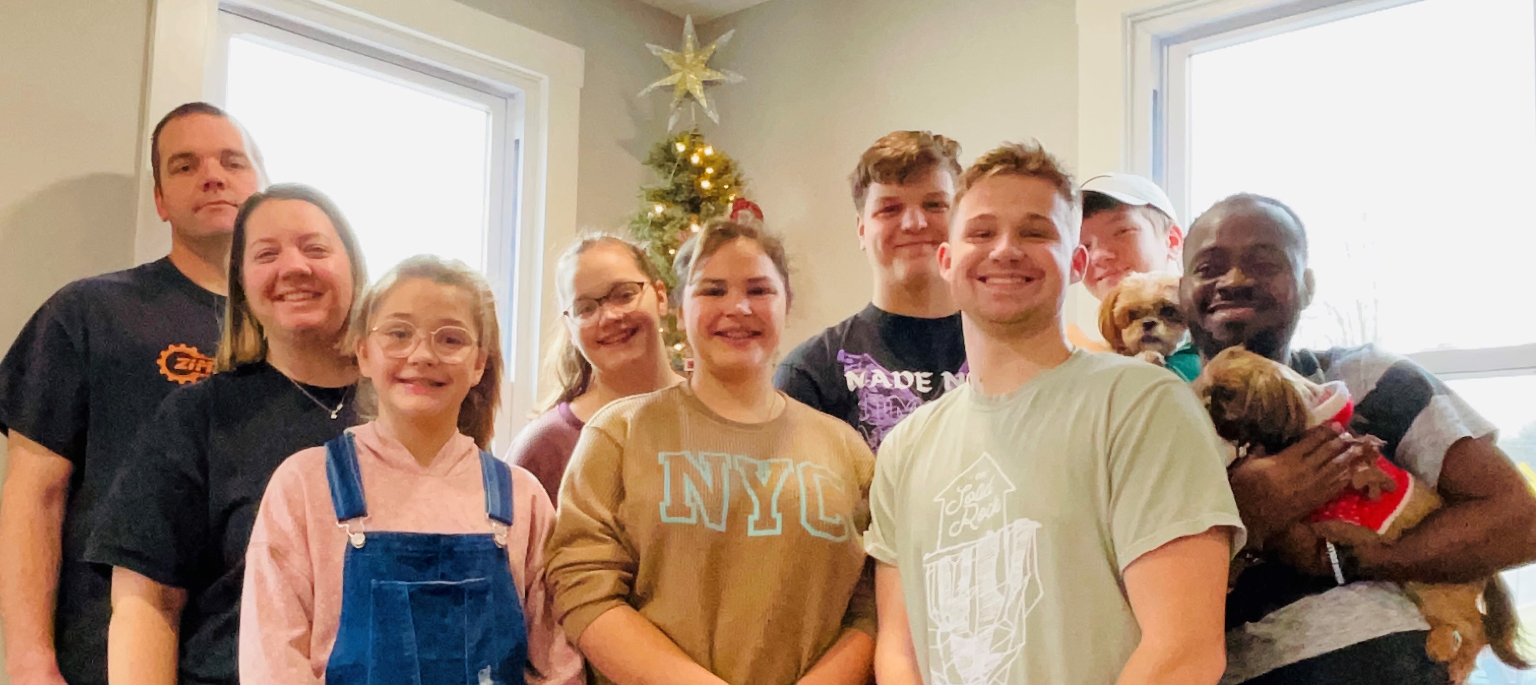 Family of eight stand with an IVEP participant in front of a Christmas tree.