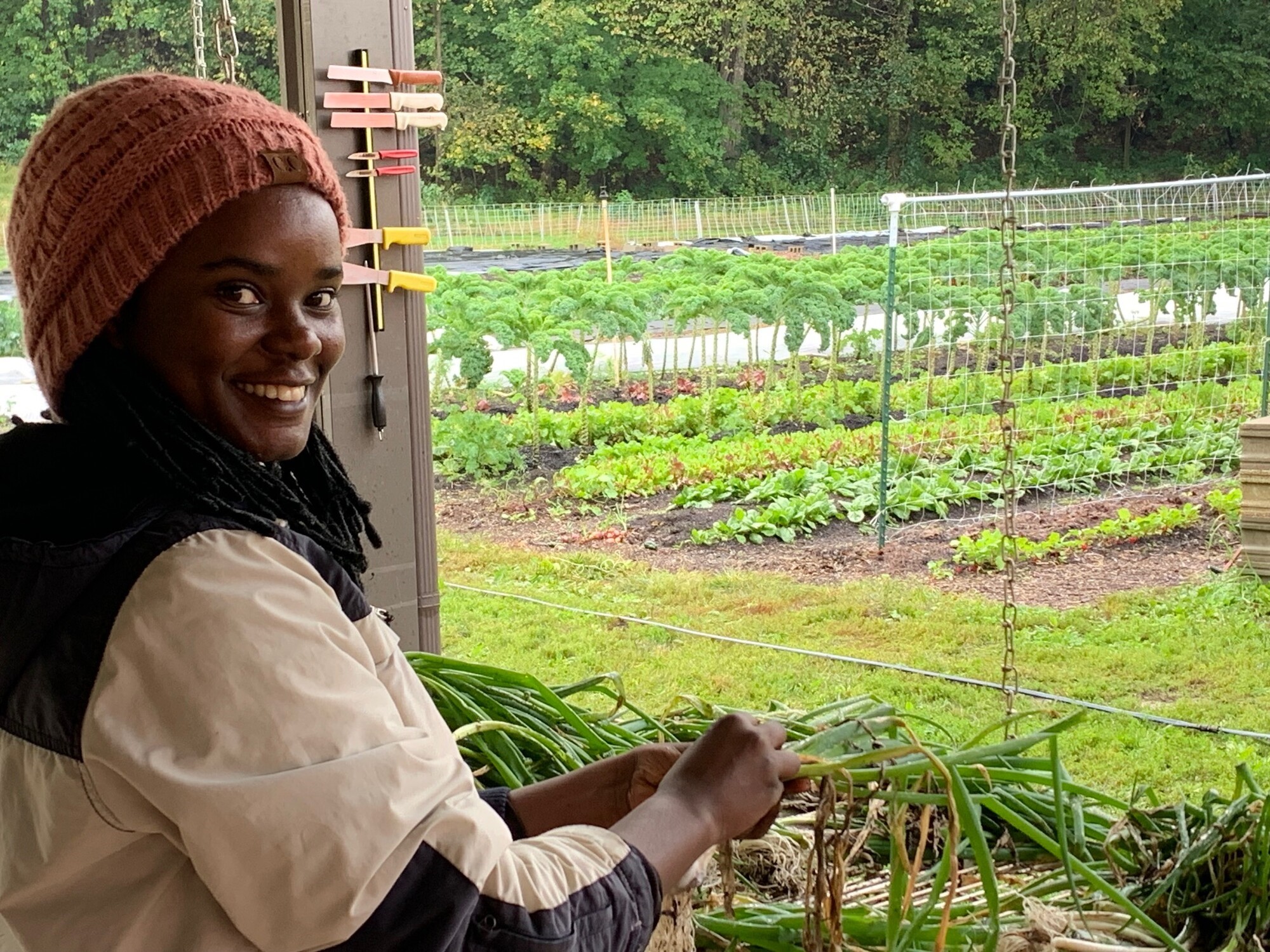 A woman holding onions with a farm in the background