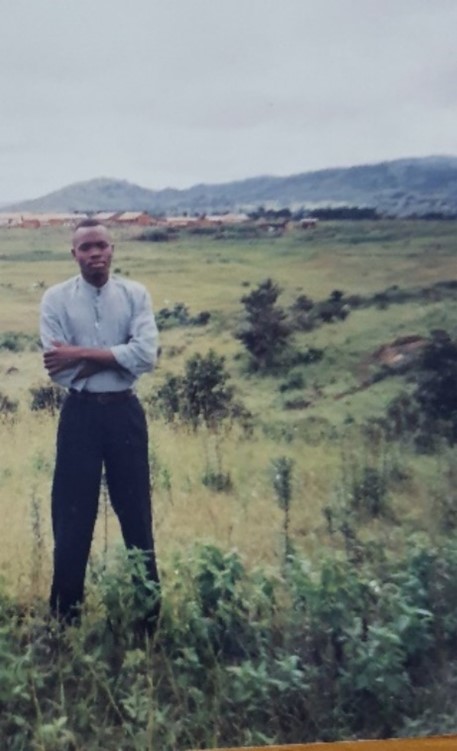 Person standing om a green and yellow field with arms crossed and hills in the background.