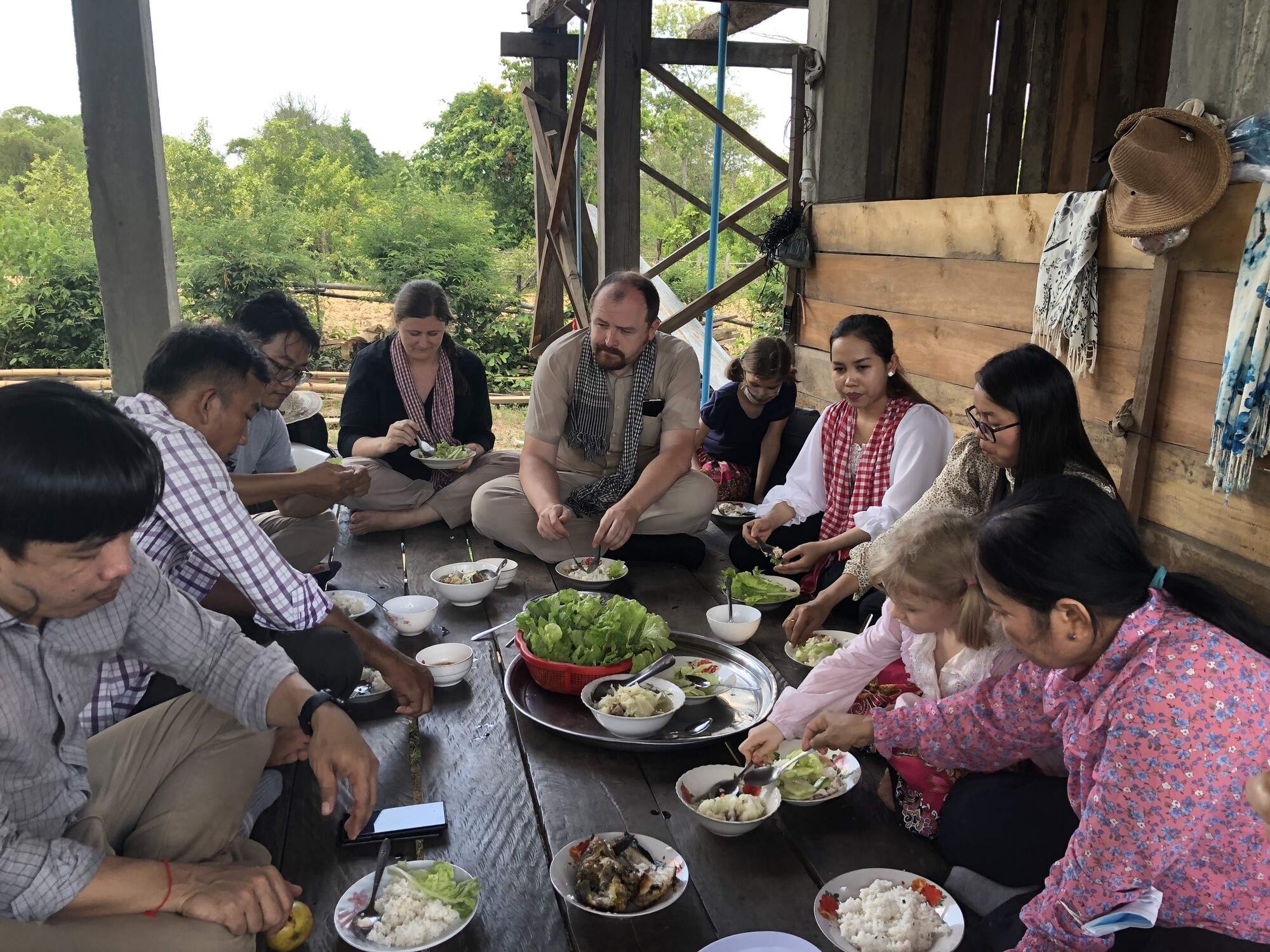 A group of ten people sit on a wooden floor eating together.