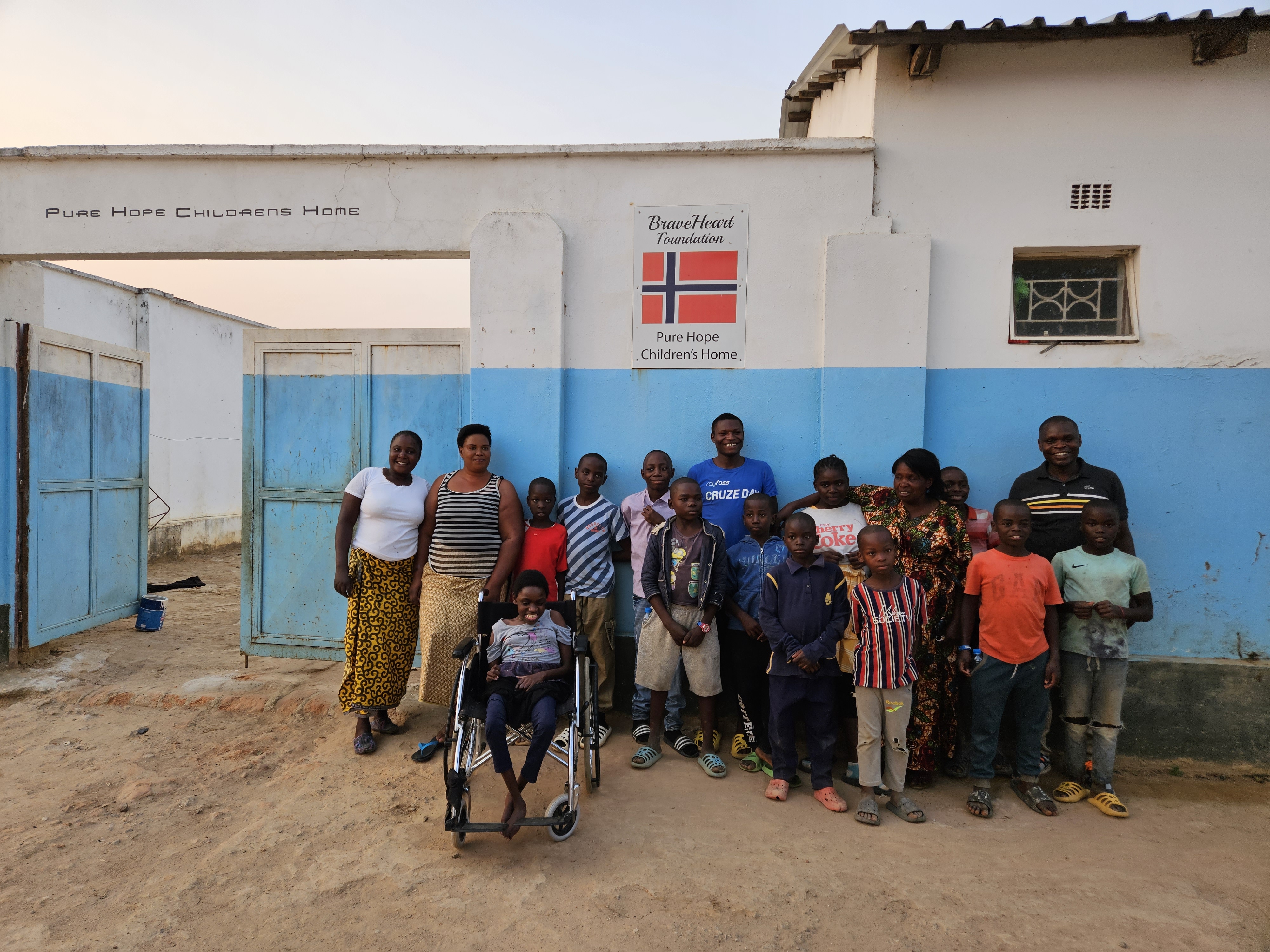 Young residents of Pure Hope Children's Home and their caretakers stand outside the organization's building, located in Meheba Refugee Settlement Camp.