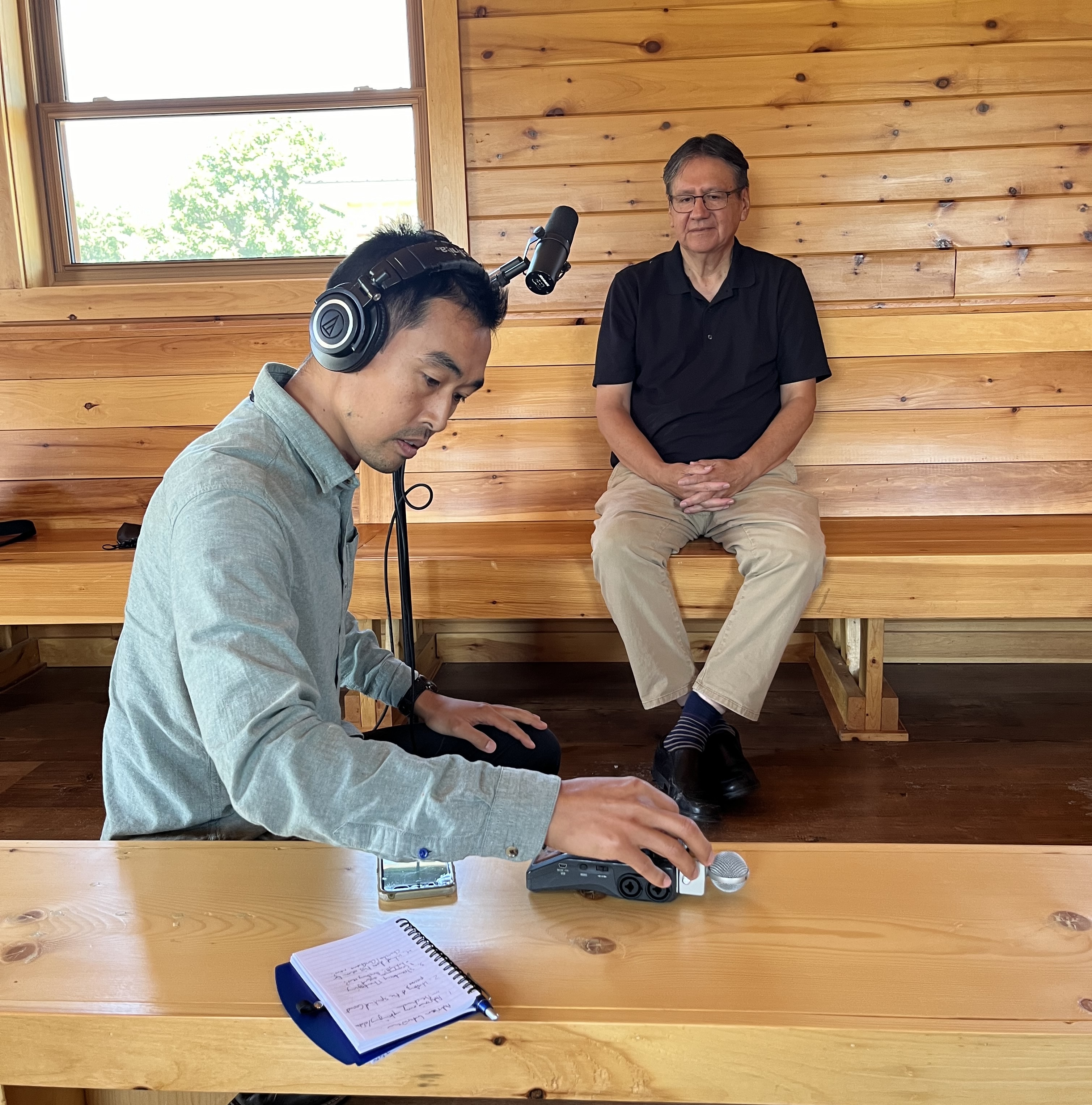 Man in green shirt adjusts sound recording while man in black shirt waits beside a microphone