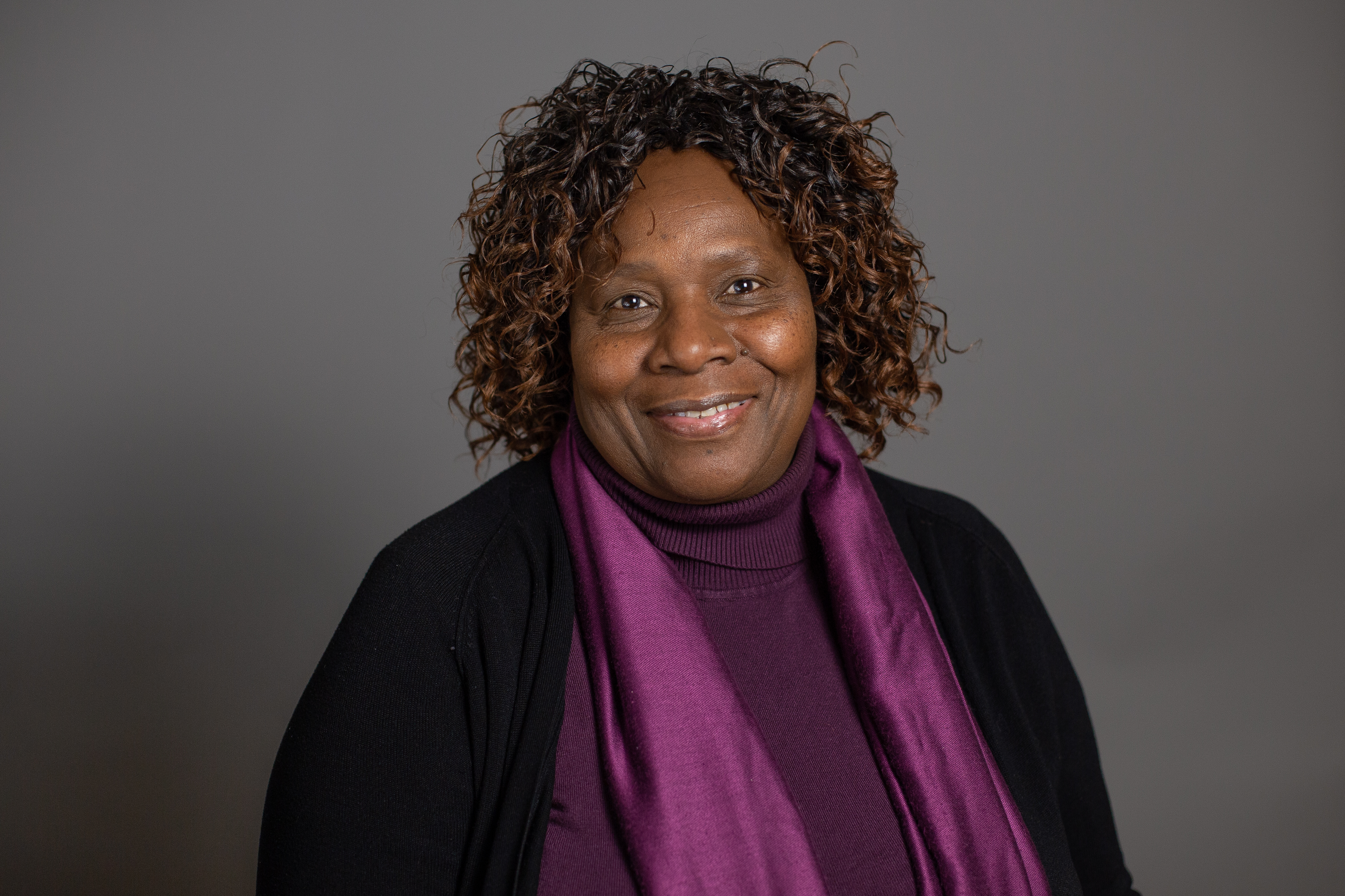 Jane Njogu, smiling in front of a grey backdrop.