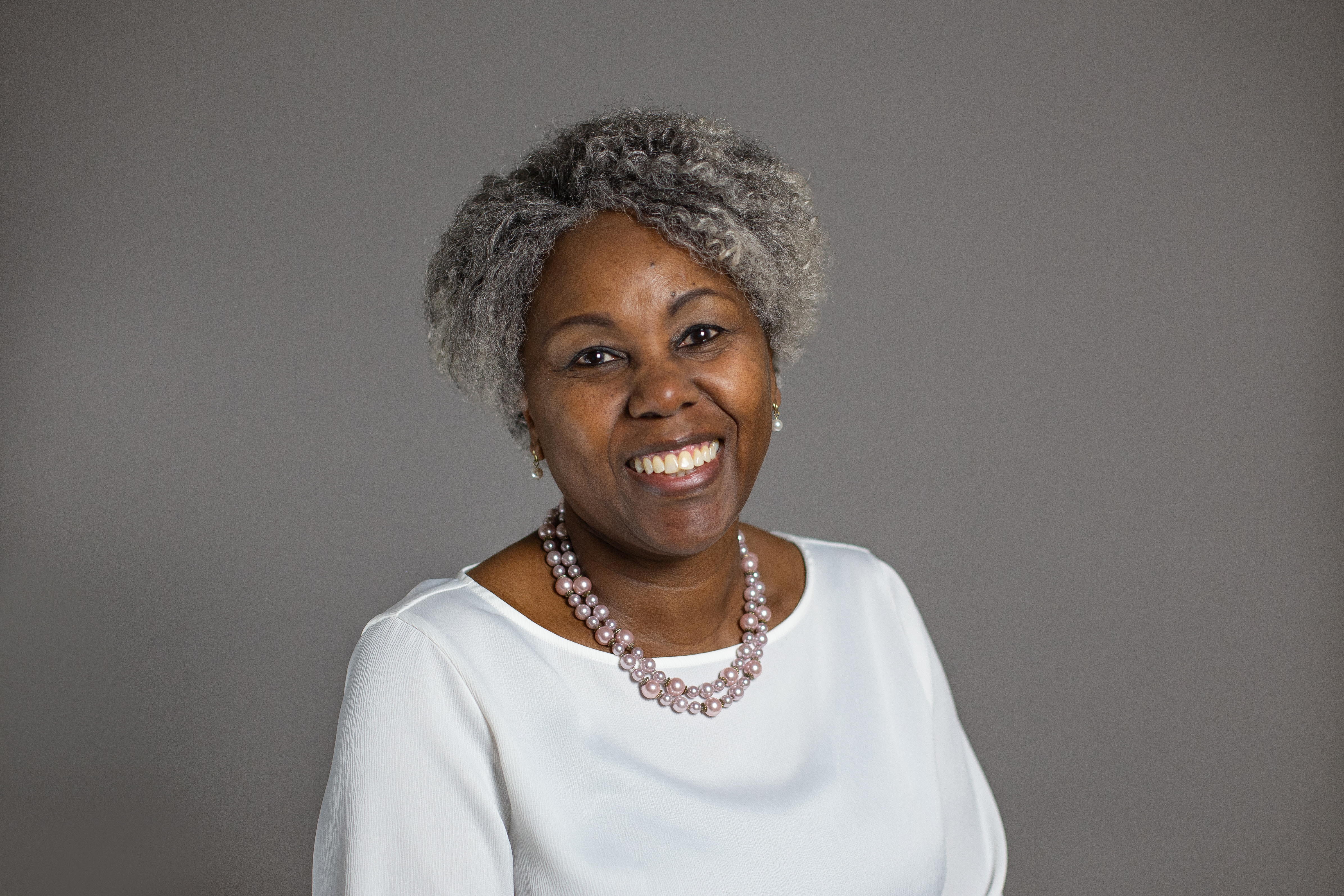 Jennifer Mpungu, smiling in front of a grey backdrop.