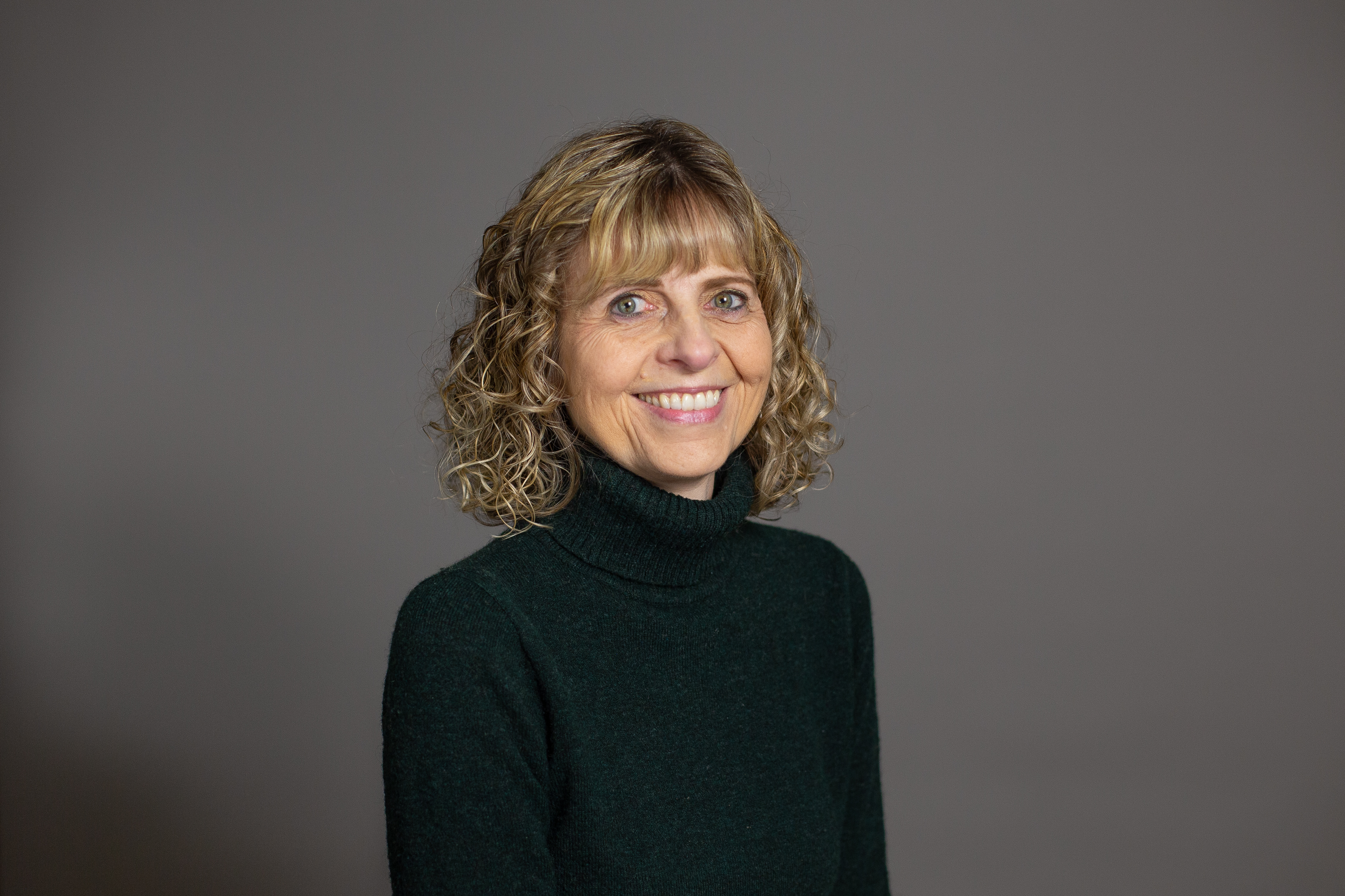 Karen Heidebrecht Thiessen pictured, smiling in front of a grey backdrop.