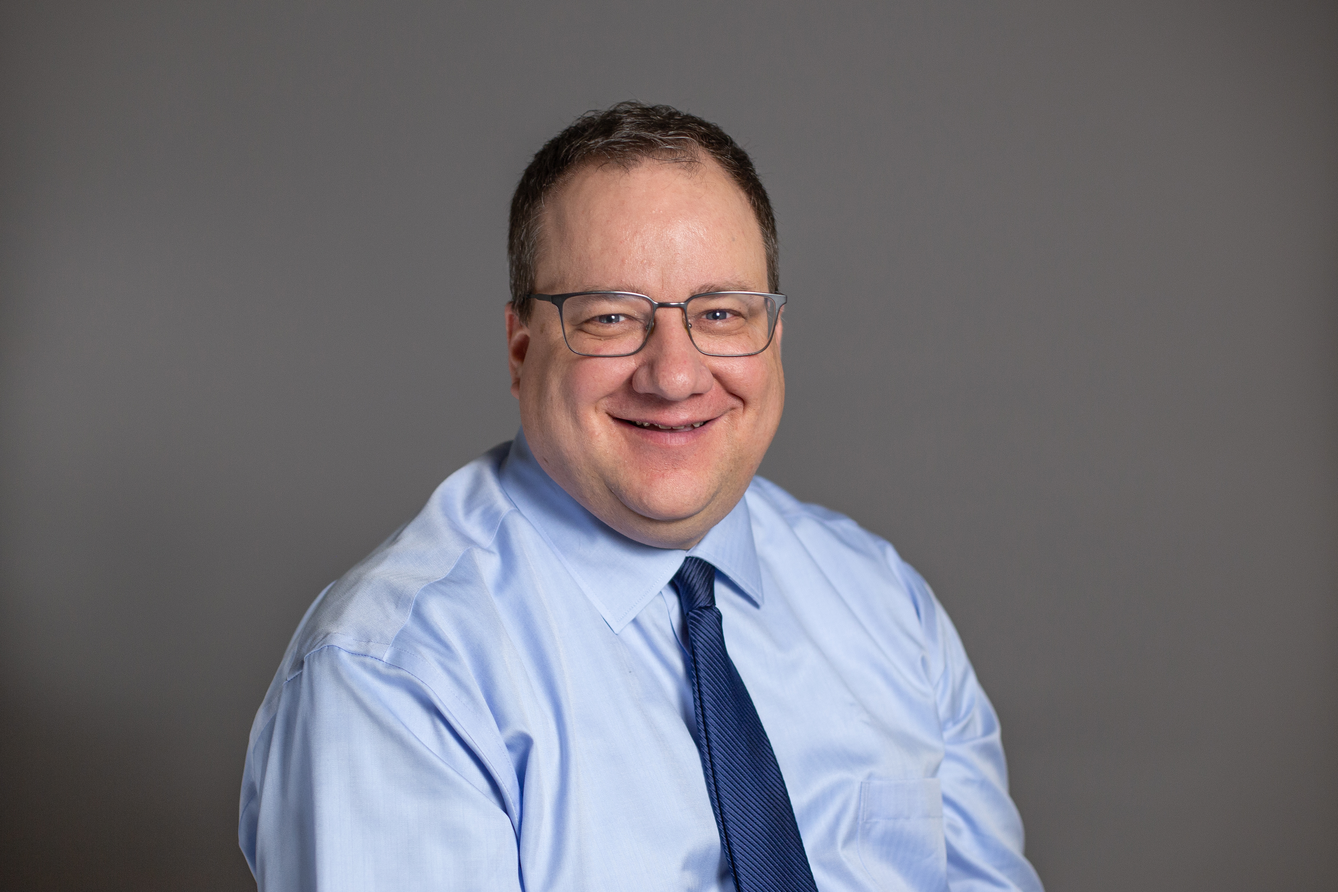 Ed Brett, smiling in front of a grey backdrop.