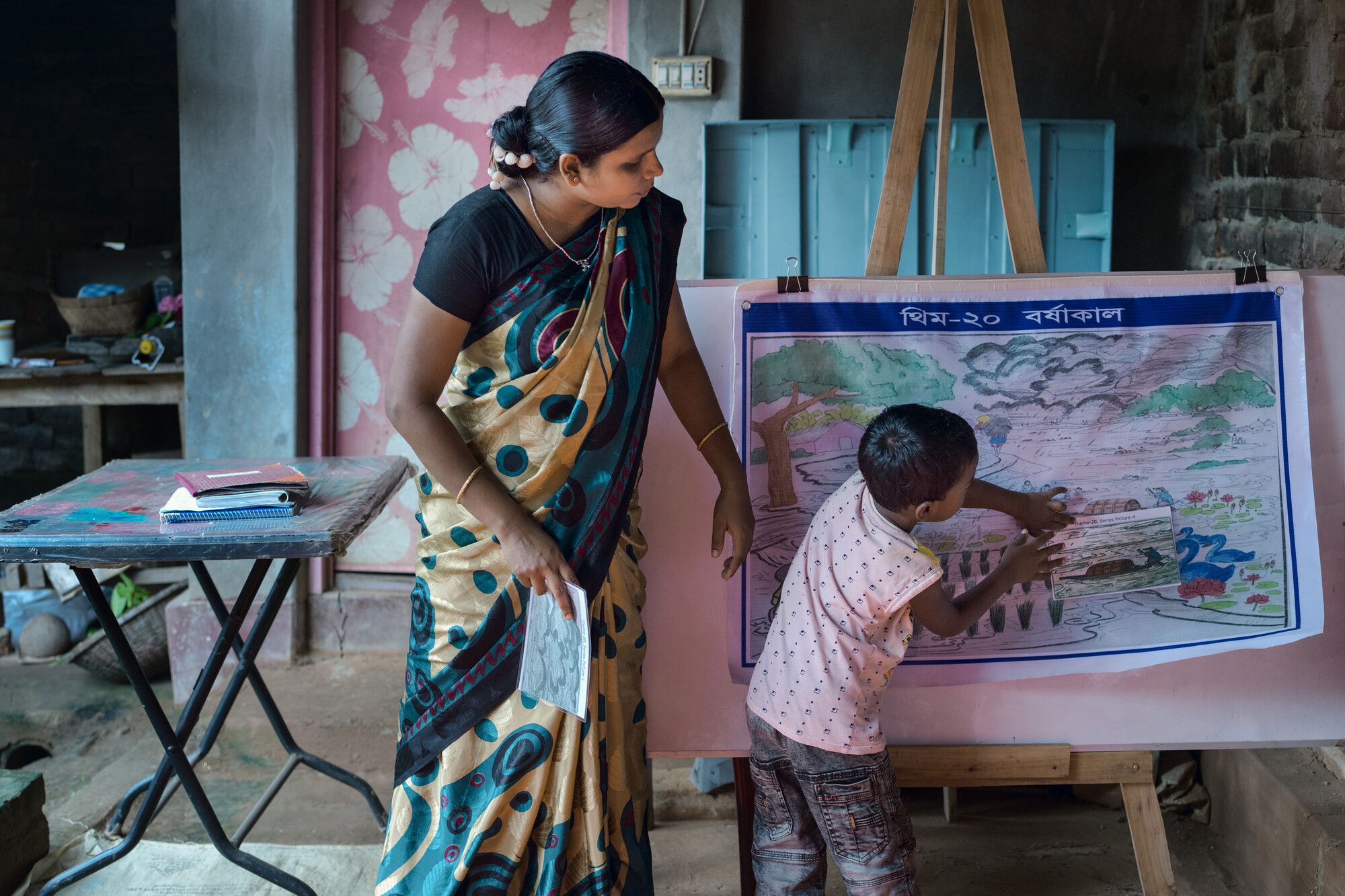 A person stands next to a child who is drawing on an easel.