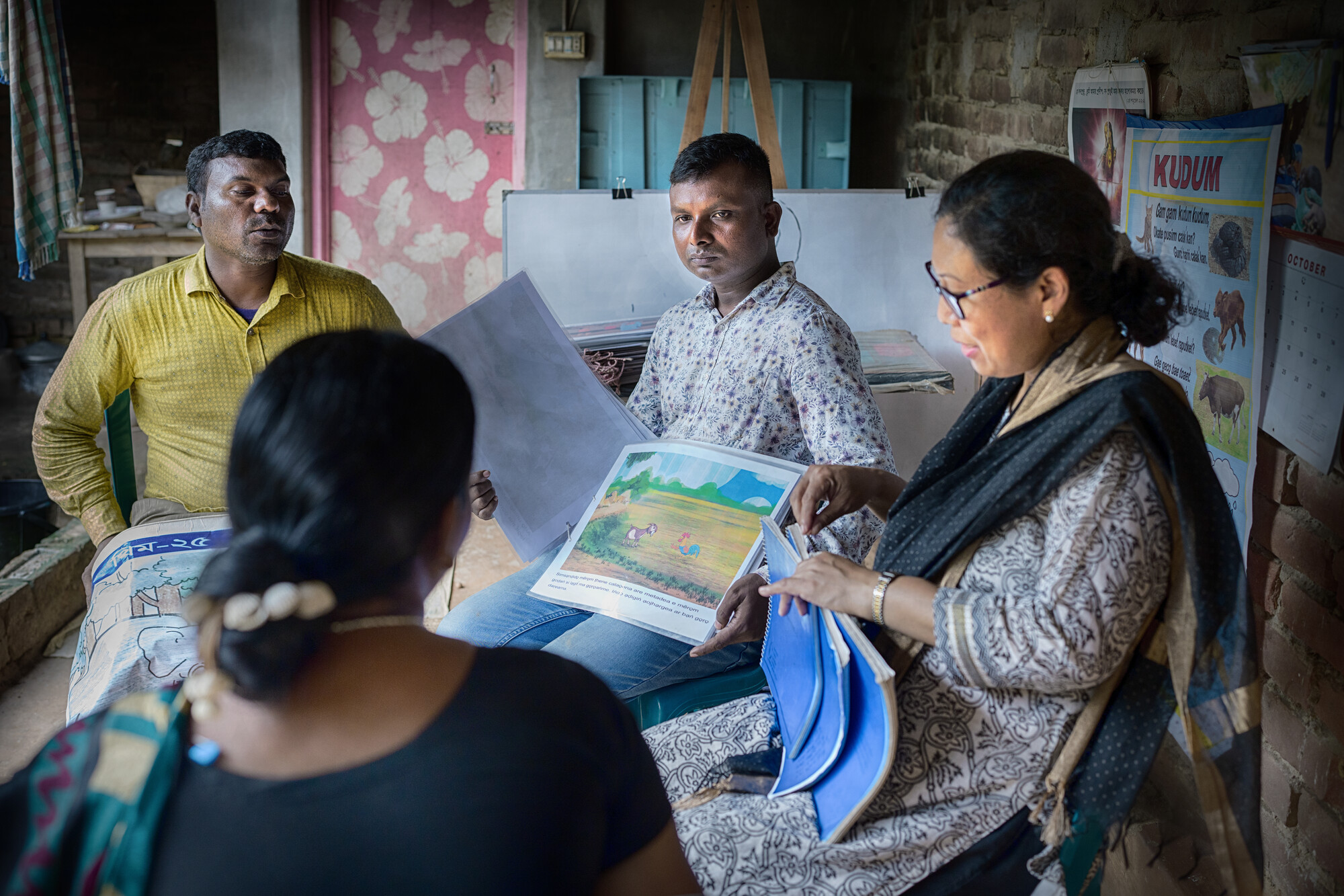 Four adults sit together, holding school curricula and conversing.