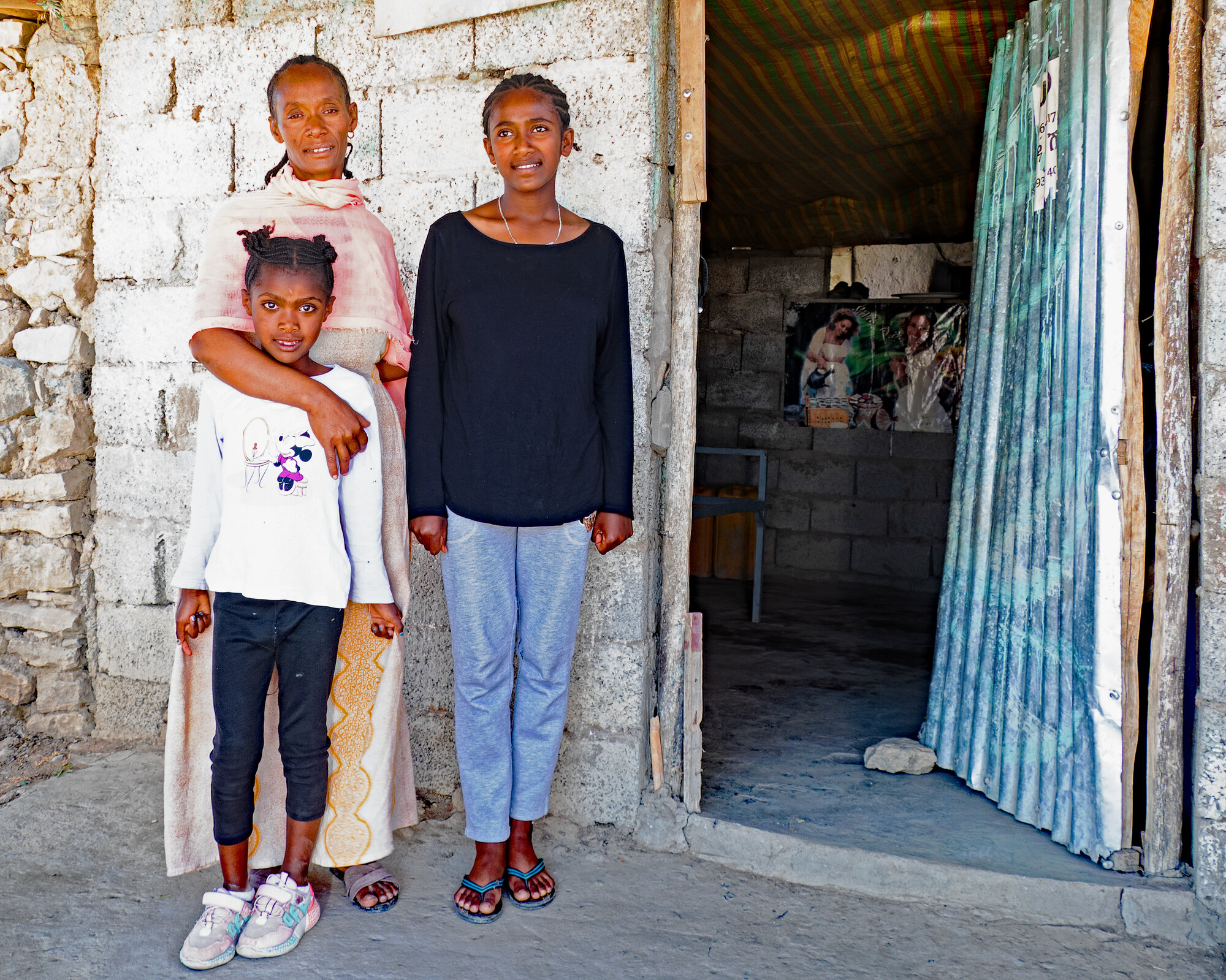 Three people stand outside a building - presumably their family home.