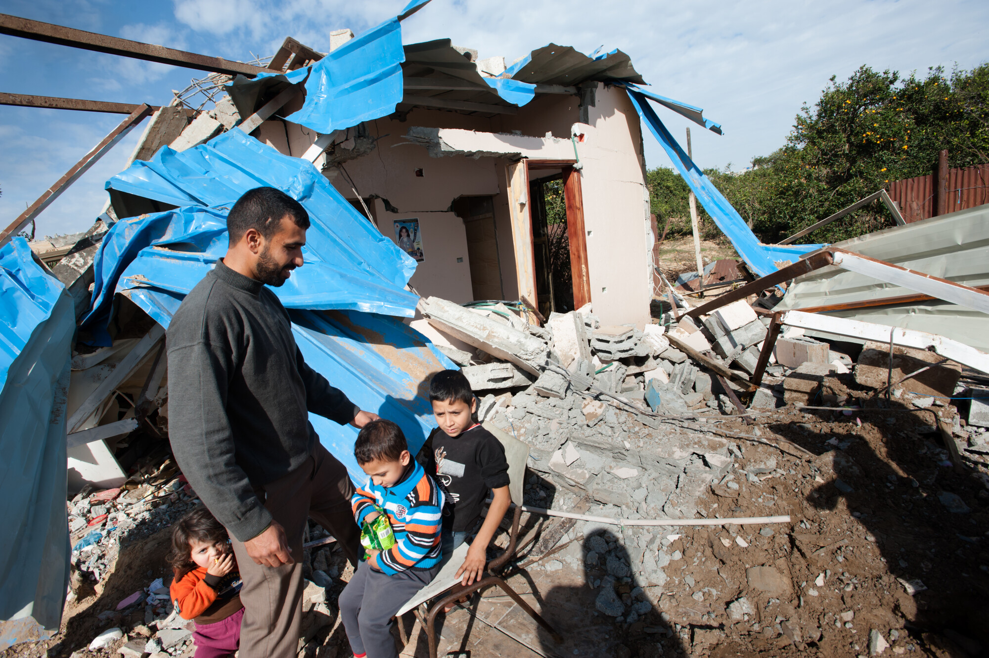 father and children in front of bombed-out house