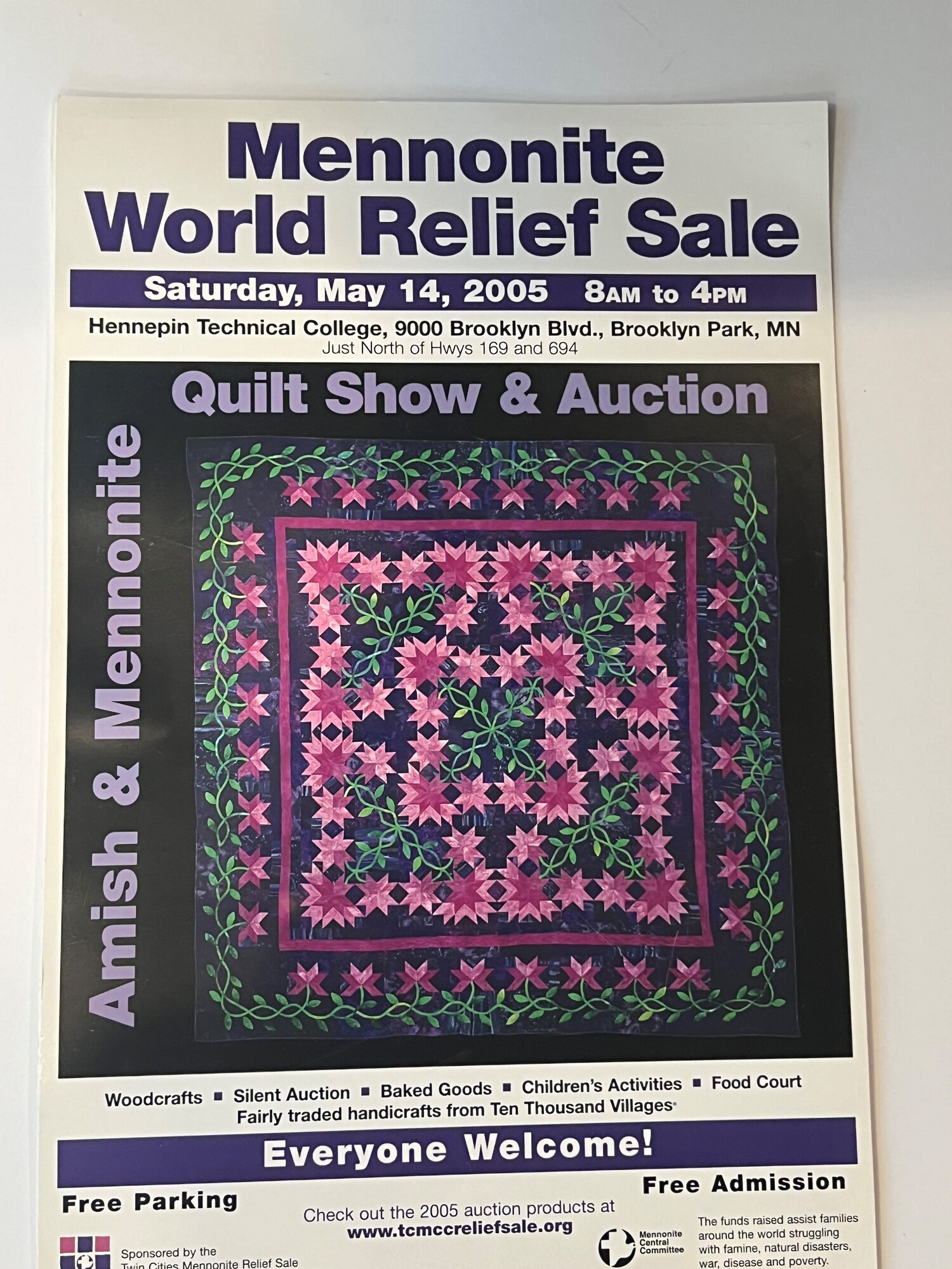 The photograph features a promotional poster for the Mennonite World Relief Sale, highlighting a quilt show and auction. It includes event details such as the date, time, and location, along with mentions of food, crafts, and children's activities.