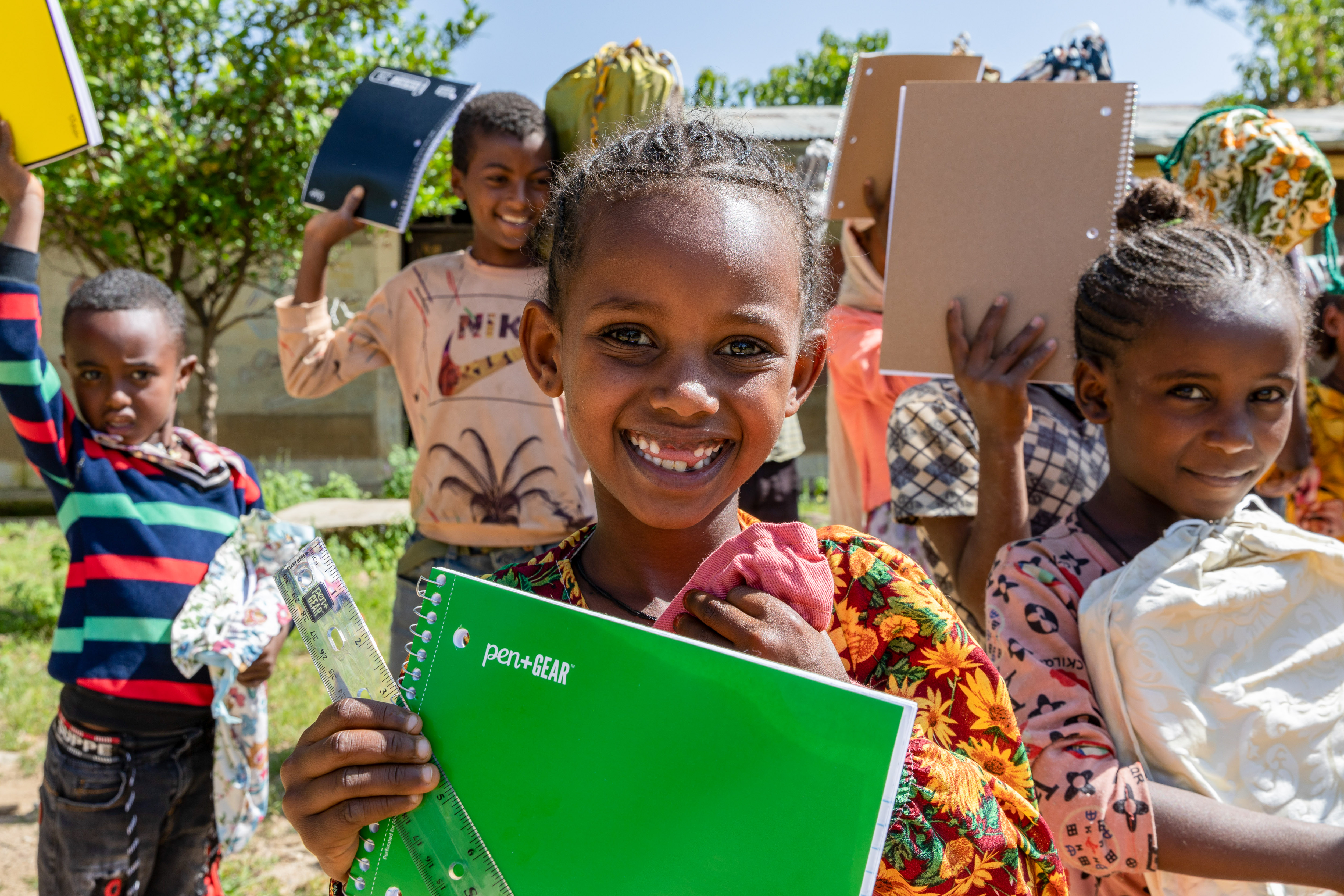 Girl holding notebook while surrounded by other students holding notebooks.