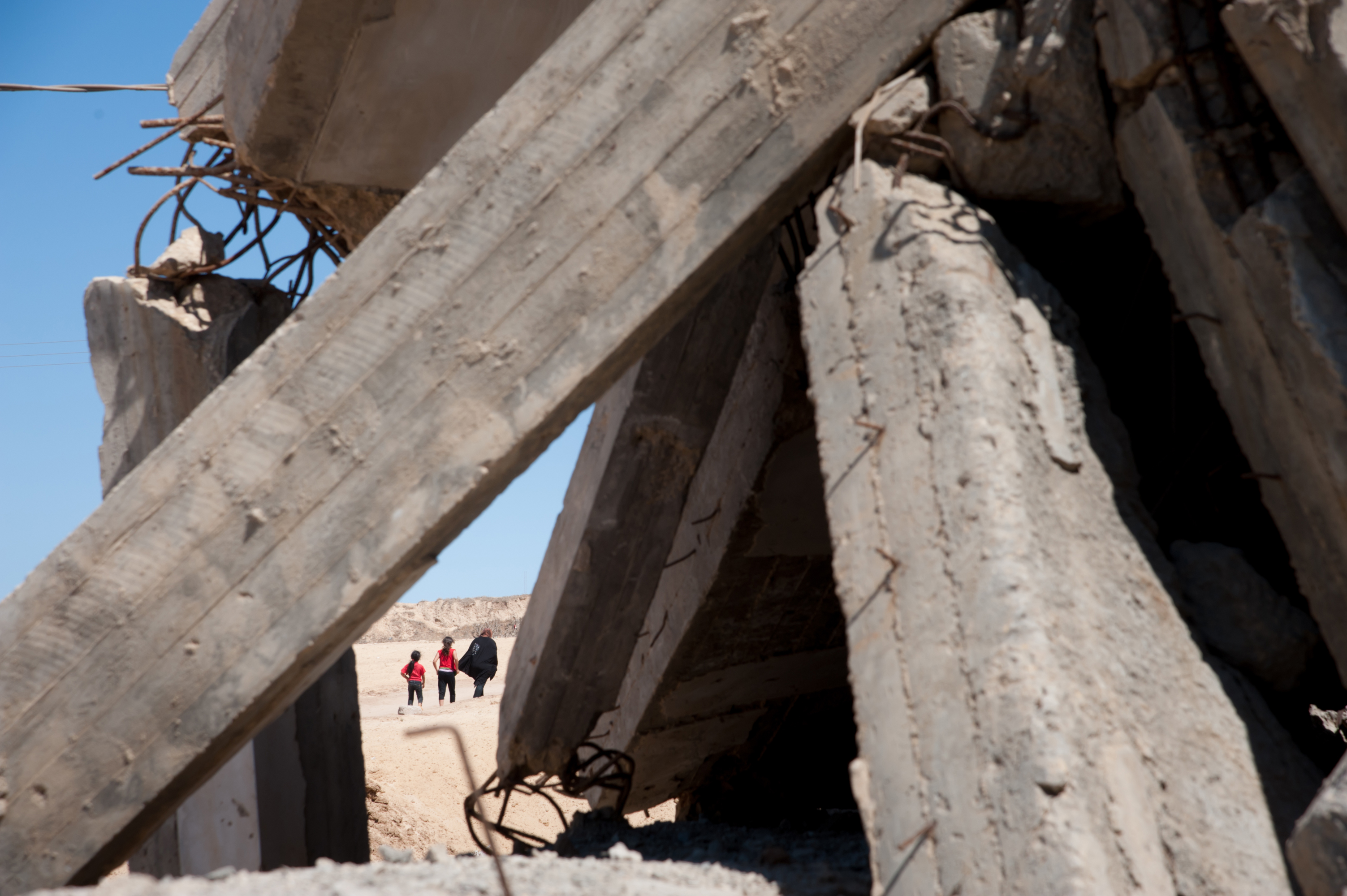 people walking in desert behind bombed cement structure