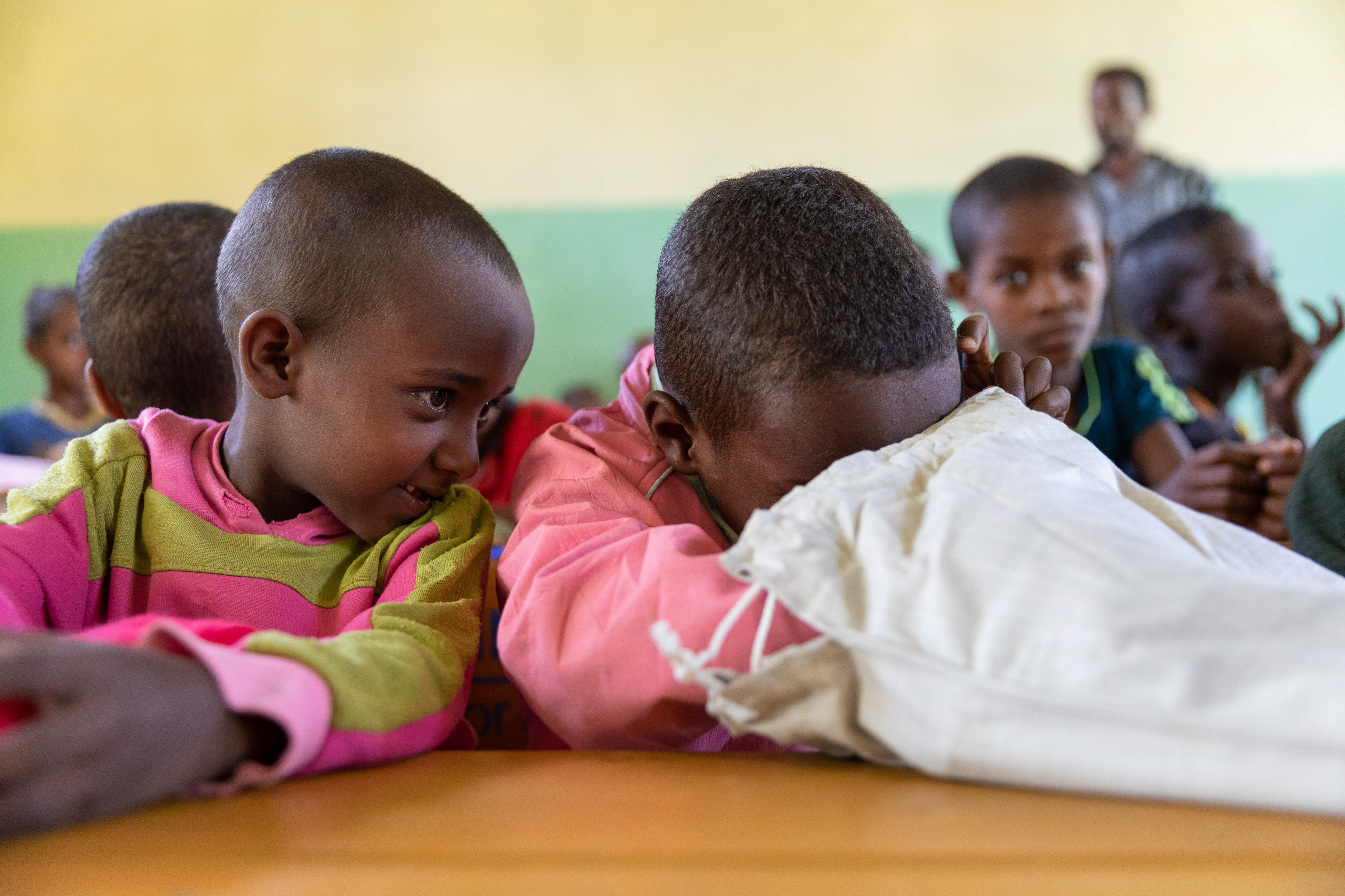 two children sitting at desk peeking into cloth bag