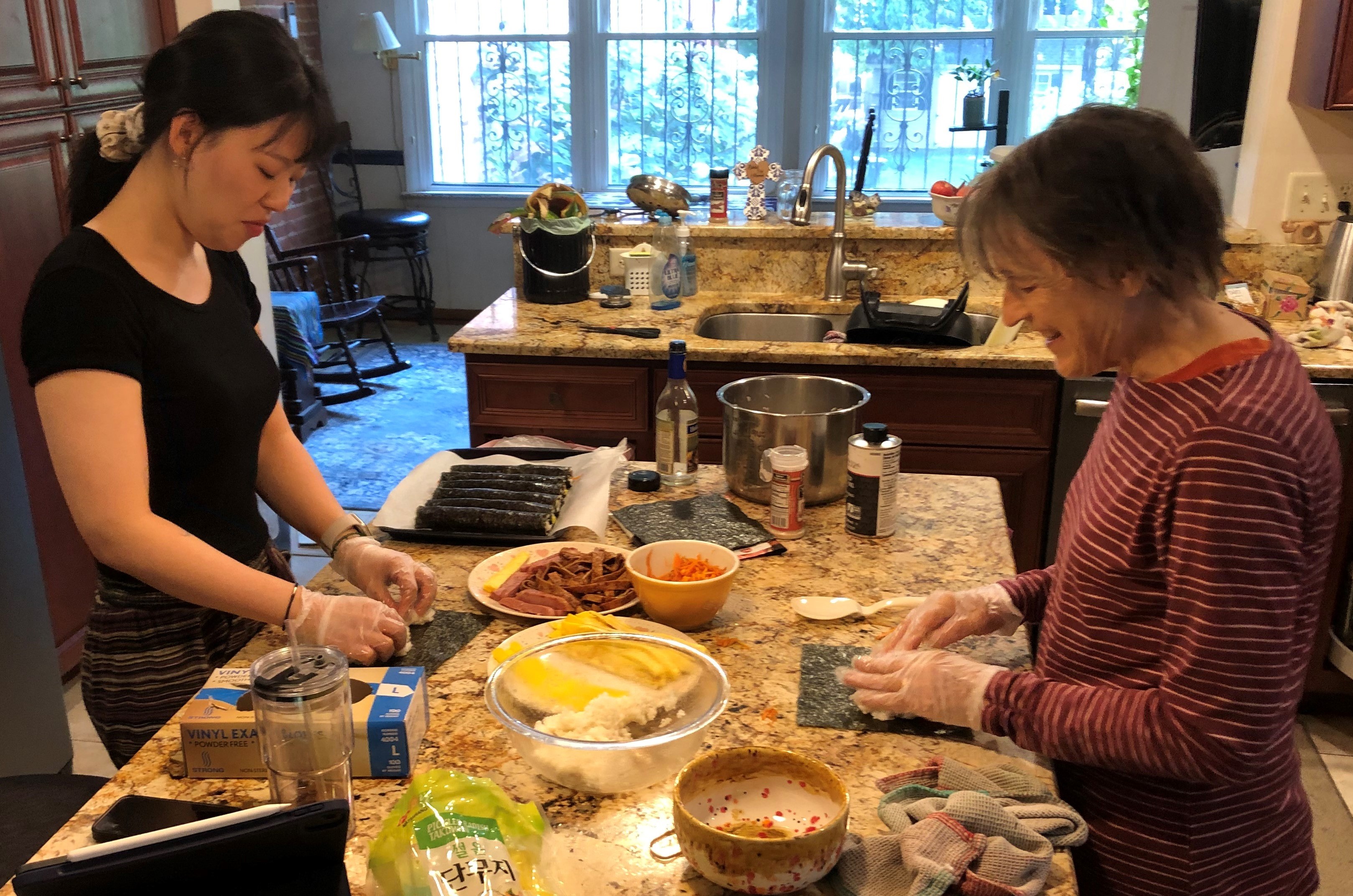 Two people stand at a kitchen island making Korean rolls called kimbap.