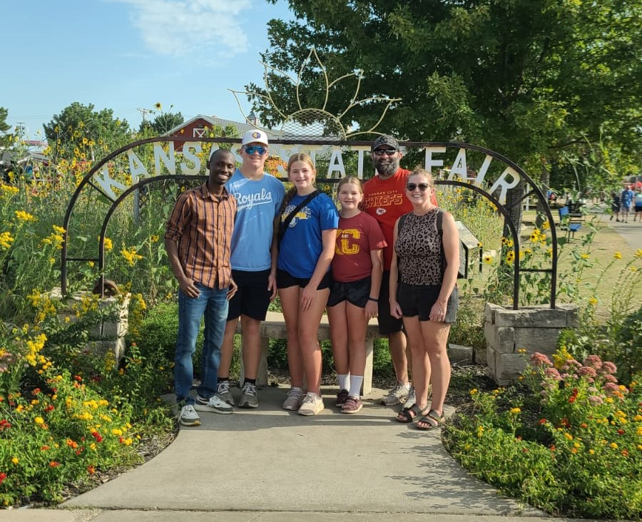 Six people stand in front of a metal sign that says "Kansas State Fair."