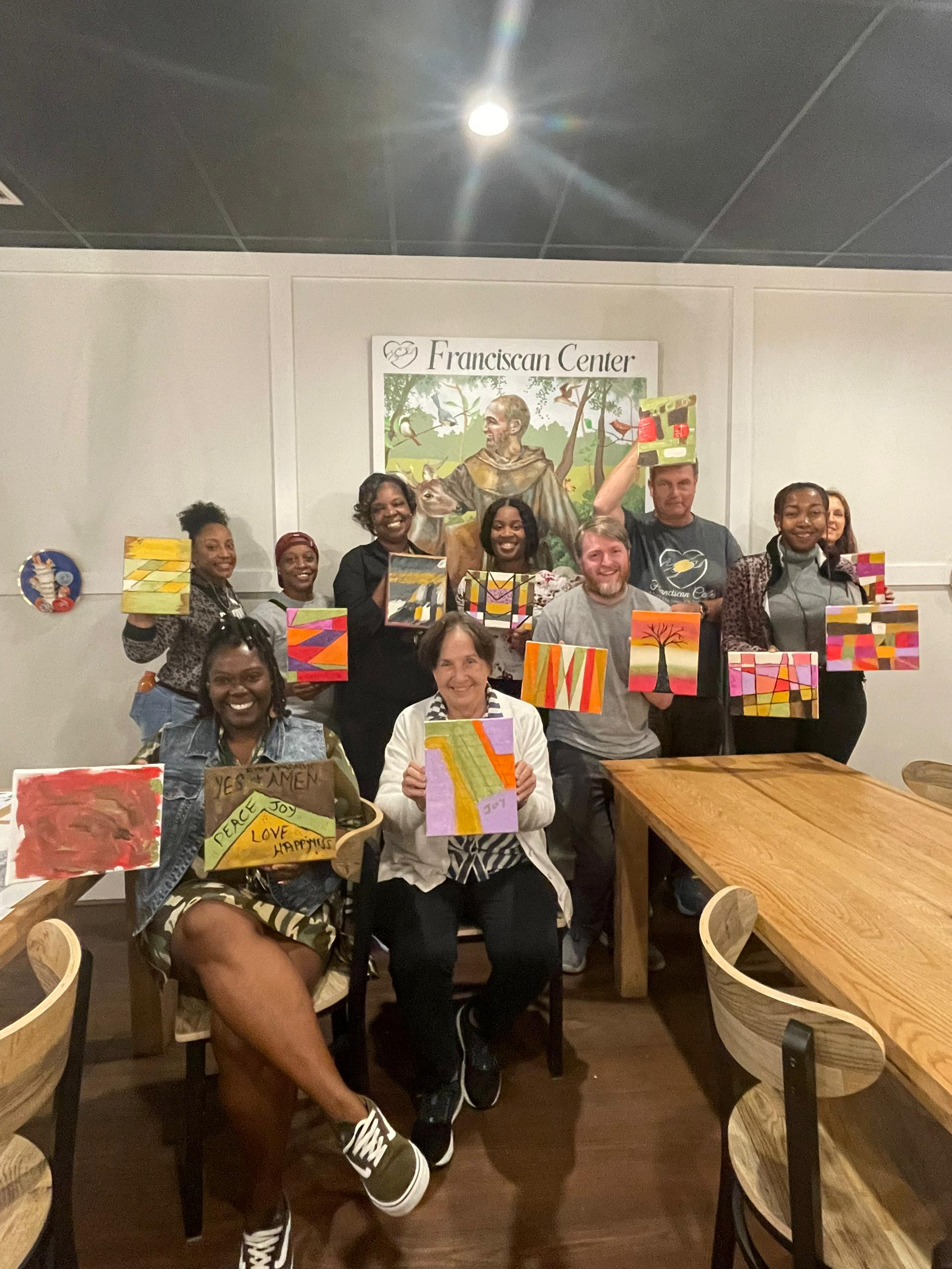 Ten people stand together presenting their paintings to the camera.