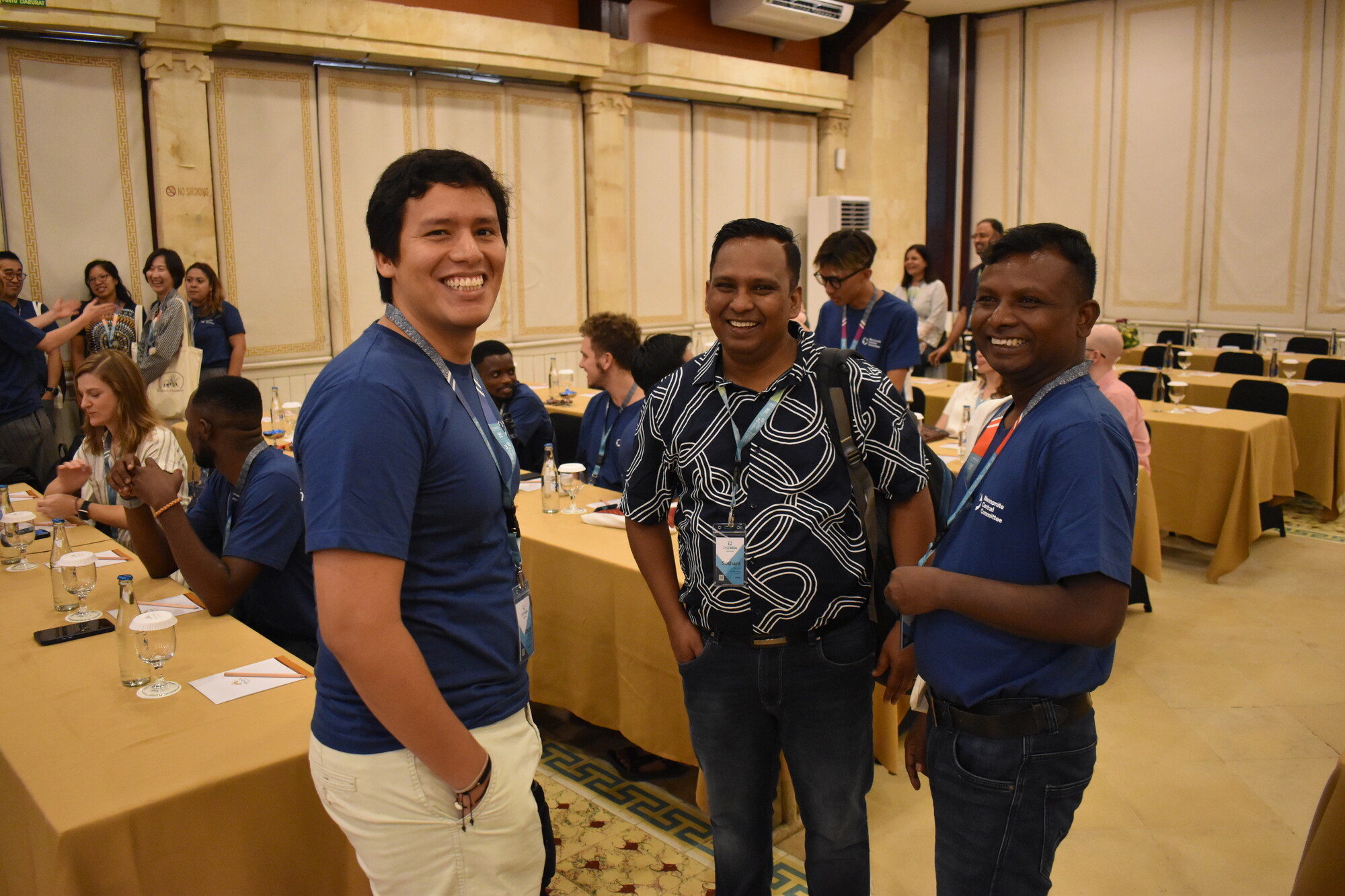 Three people wearing lanyards physically oriented toward each other in discussion smile for the camera.