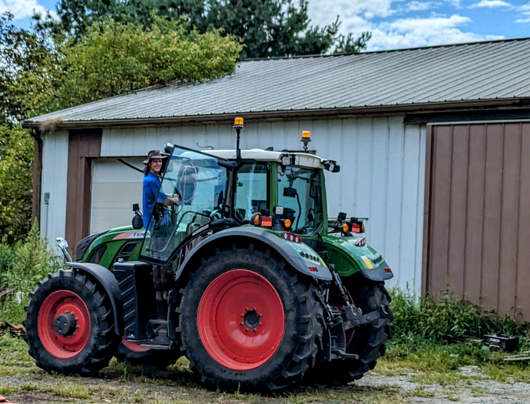 A person stands on the steps to an enormous tractor.