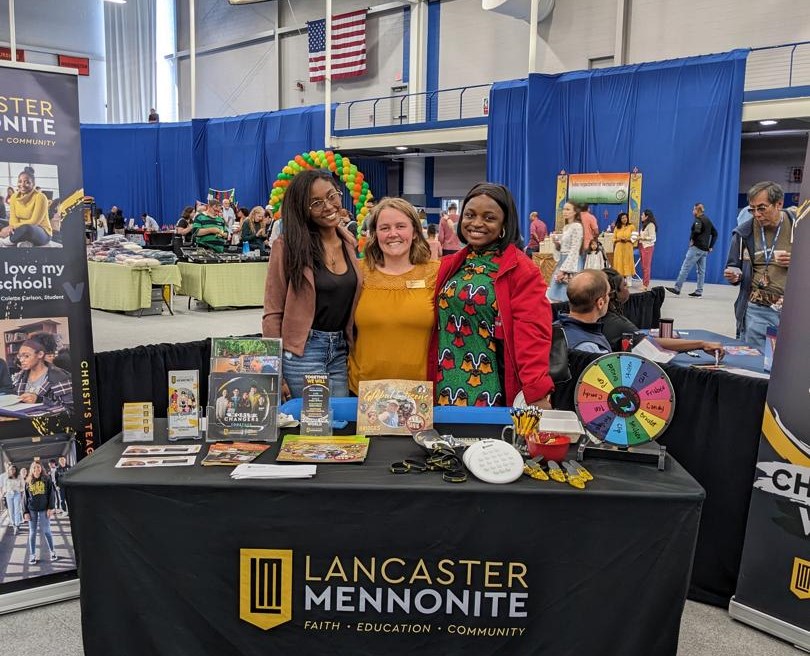 Three people stand at a recruiting table with signage for Lancaster Mennonite.