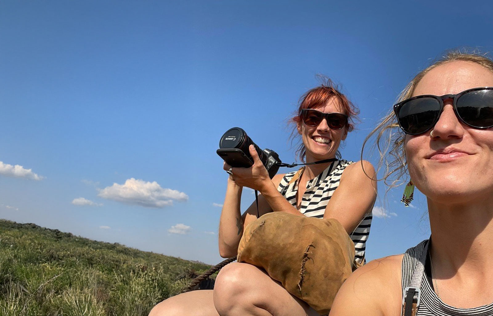 two women smiling at the camera, one holds a camera