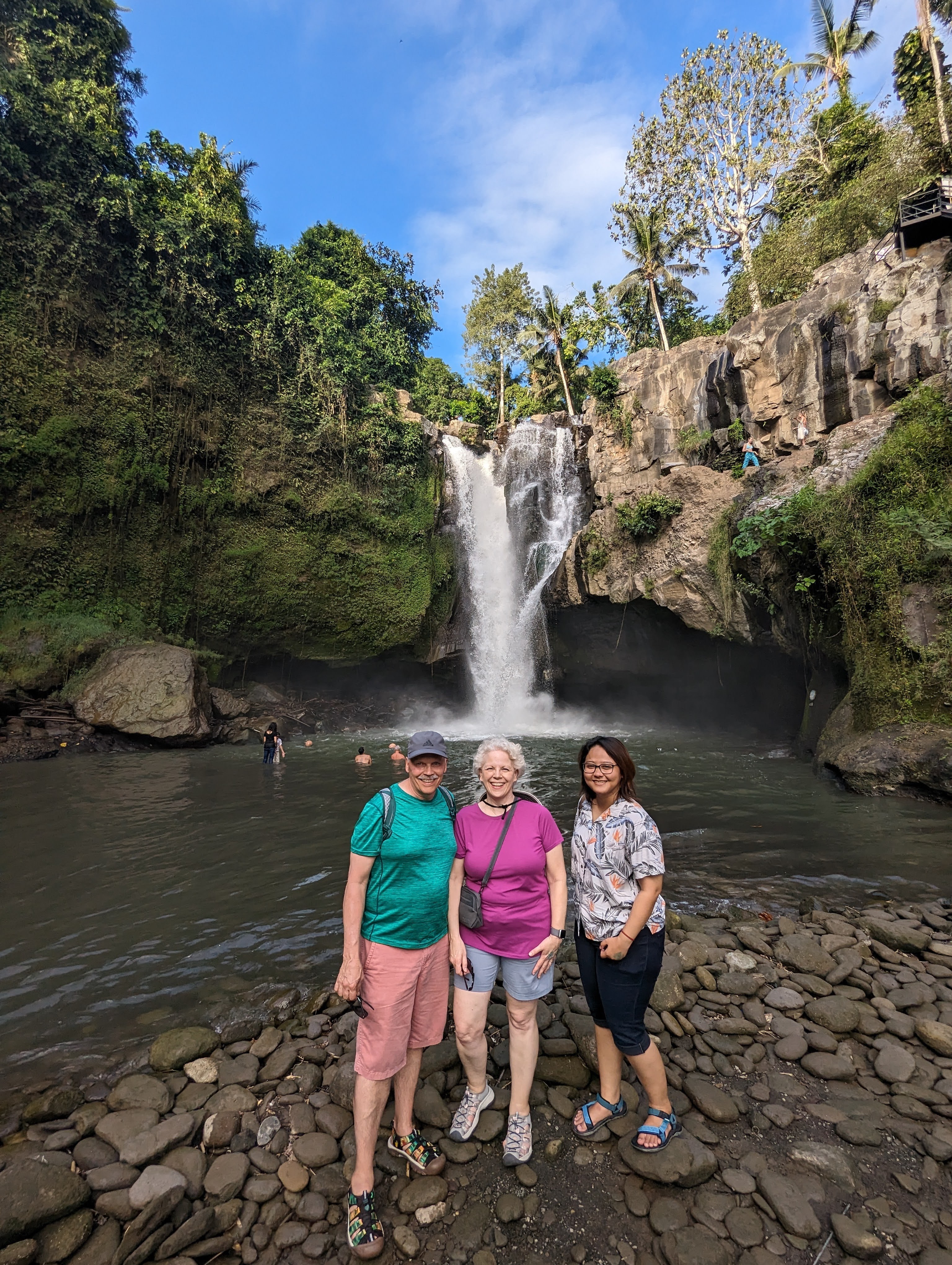 Three people stand in front of a scenic waterfall.