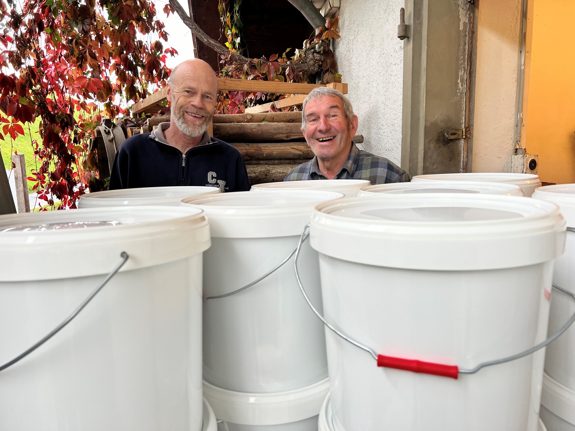 Two men standing behind a pile of oversize buckets with lids