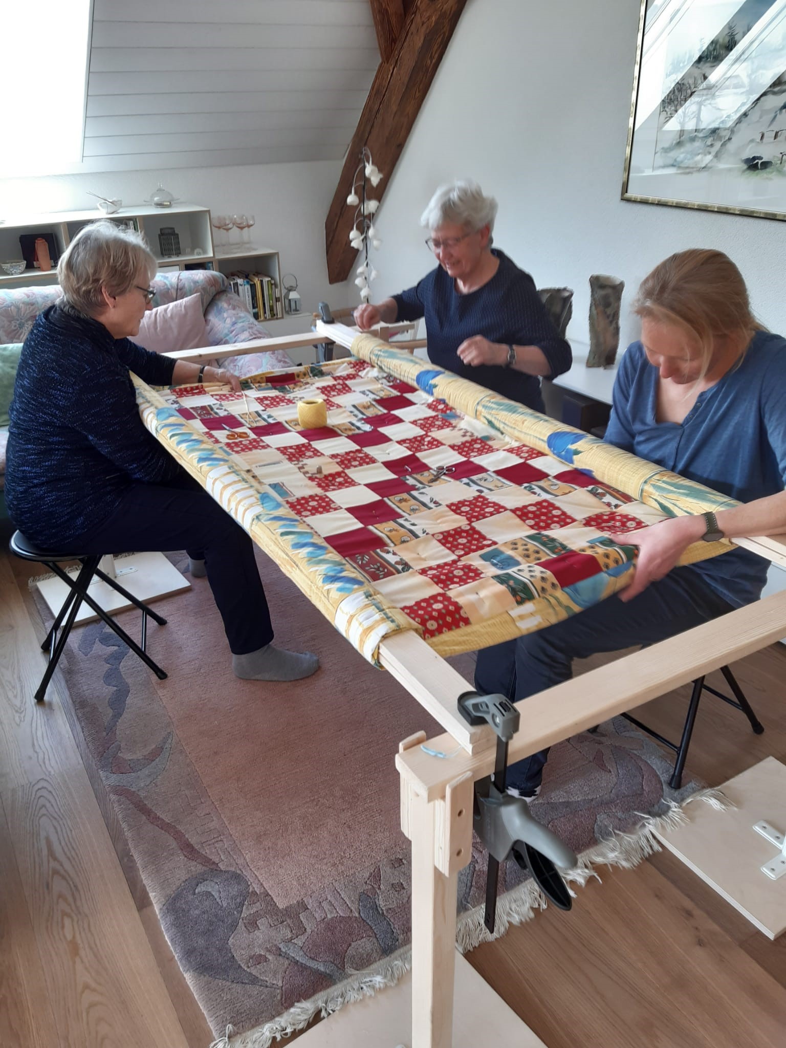 women sitting around table and knotting a comforter