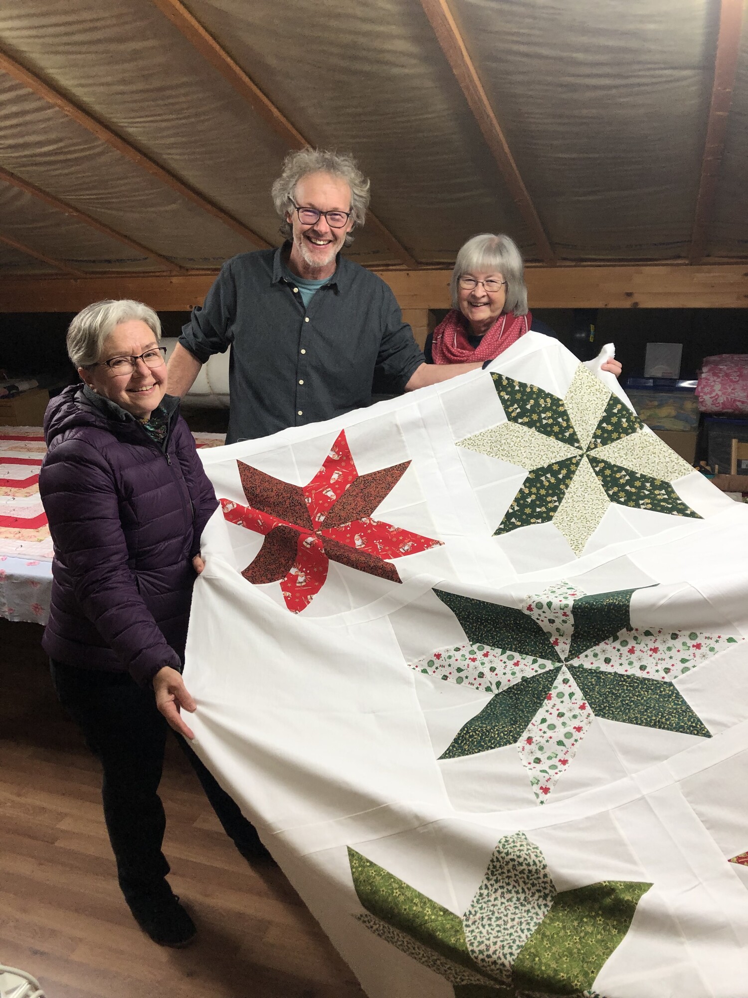 three people standing and displaying a comforter