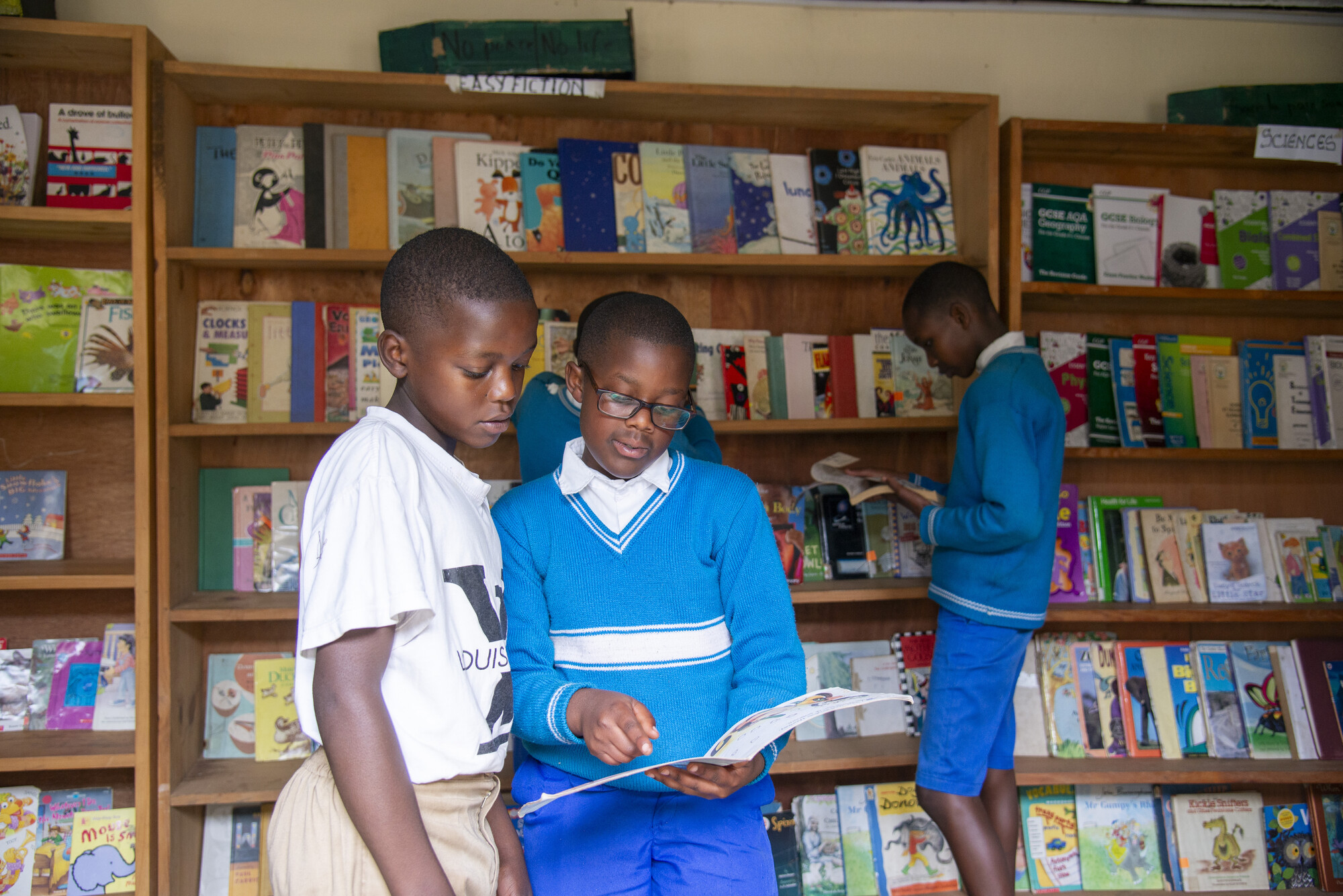 Jean d'Amour Iravuze, left, and Bruno Ineza Kabera read a book at the Gicumbi Children's Peace Library, operated by Transformational Leadership Center. Books are organized into categories like easy fi