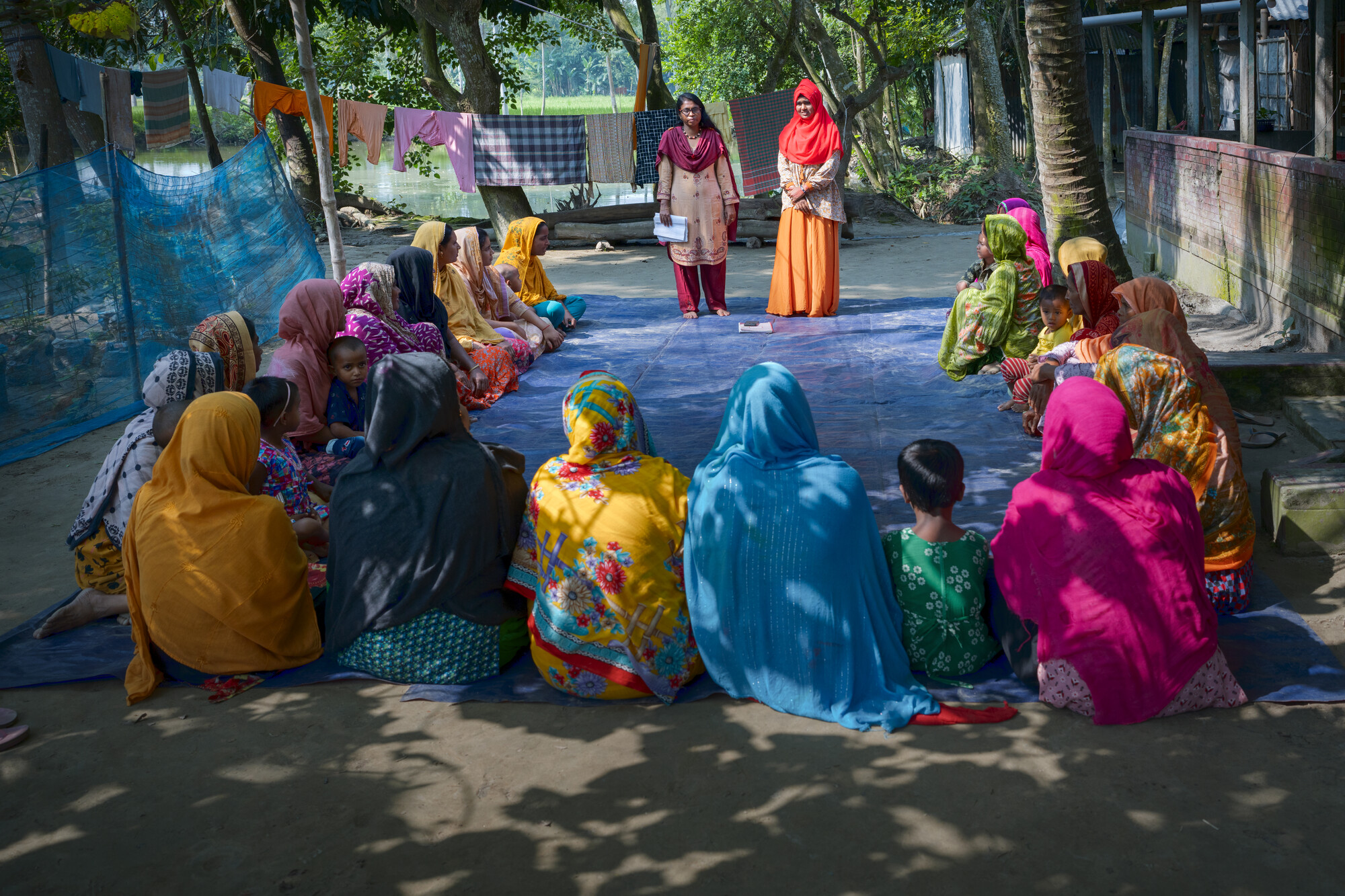 MPUS field organizers, Jannatul Naim, right, and Shamima Akter talk about the benefit of creating a hanging garden by planting vegetables in a sack at a courtyard meeting with female farmers. These tr