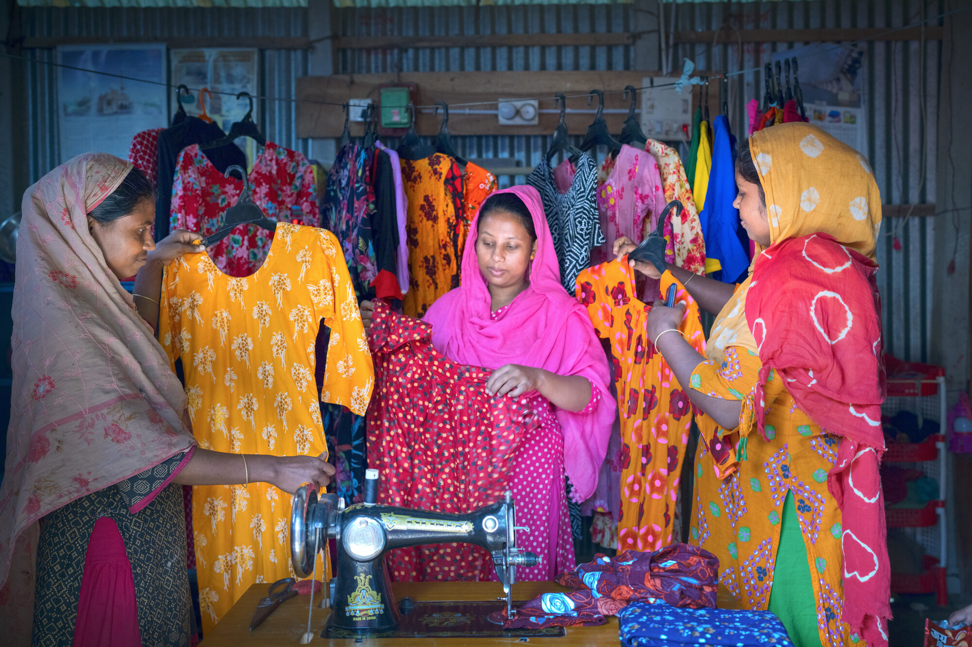 Lipi Khatun operates a business, Tanzia Tailoring, after taking sewing training and getting a sewing machine from MPUS. She stands with two of her customers, Parvin, left, who asked to use one name, a