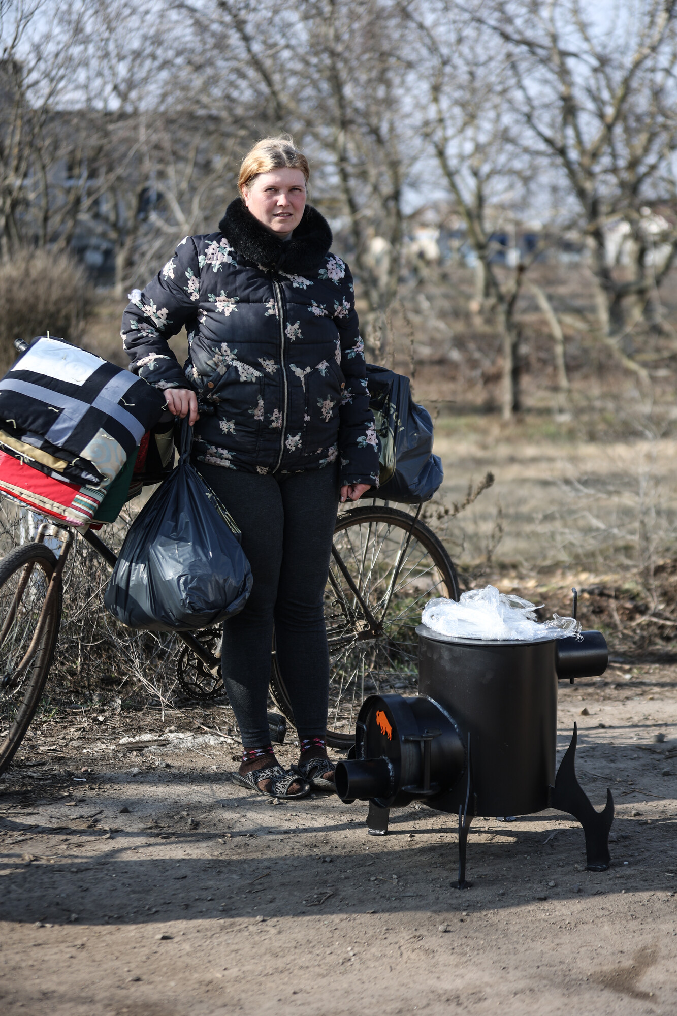 A woman* in a village recovered from Russian military control in Ukraine's Kherson region is pictured with the food packages, MCC comforter and wood stove she received from MCC partner Charitable Foun