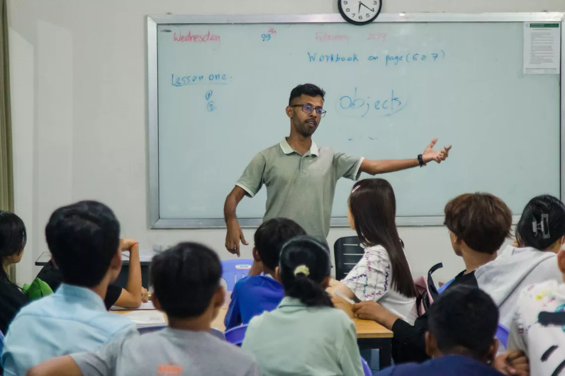 A person stands in front of a whiteboard gesturing to a group of students.