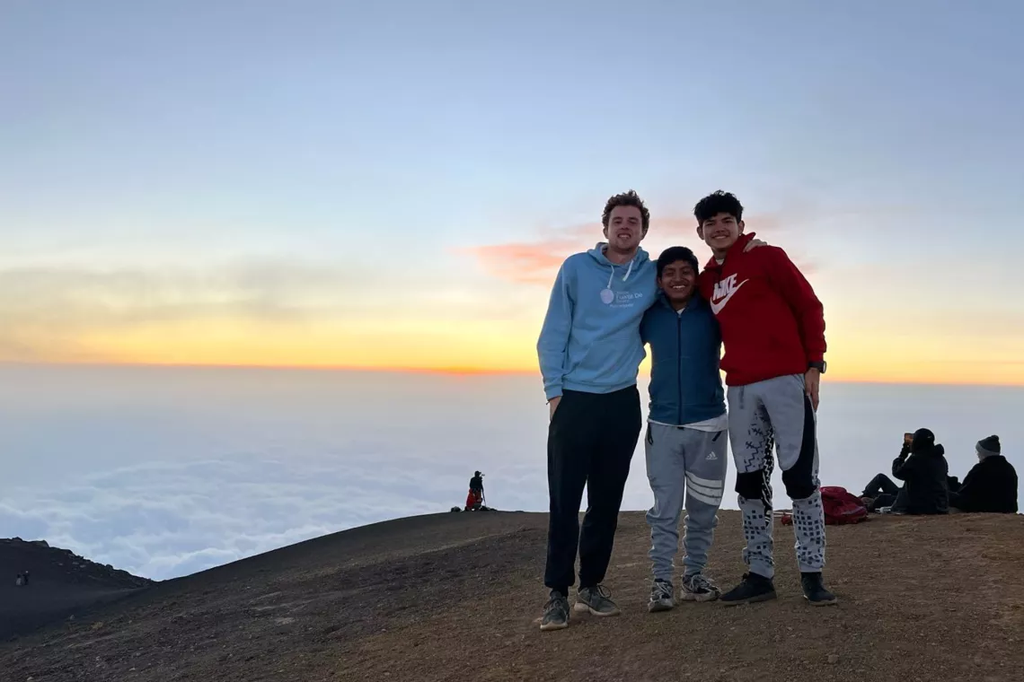 Three people stand together on top of a volcano at sunset.