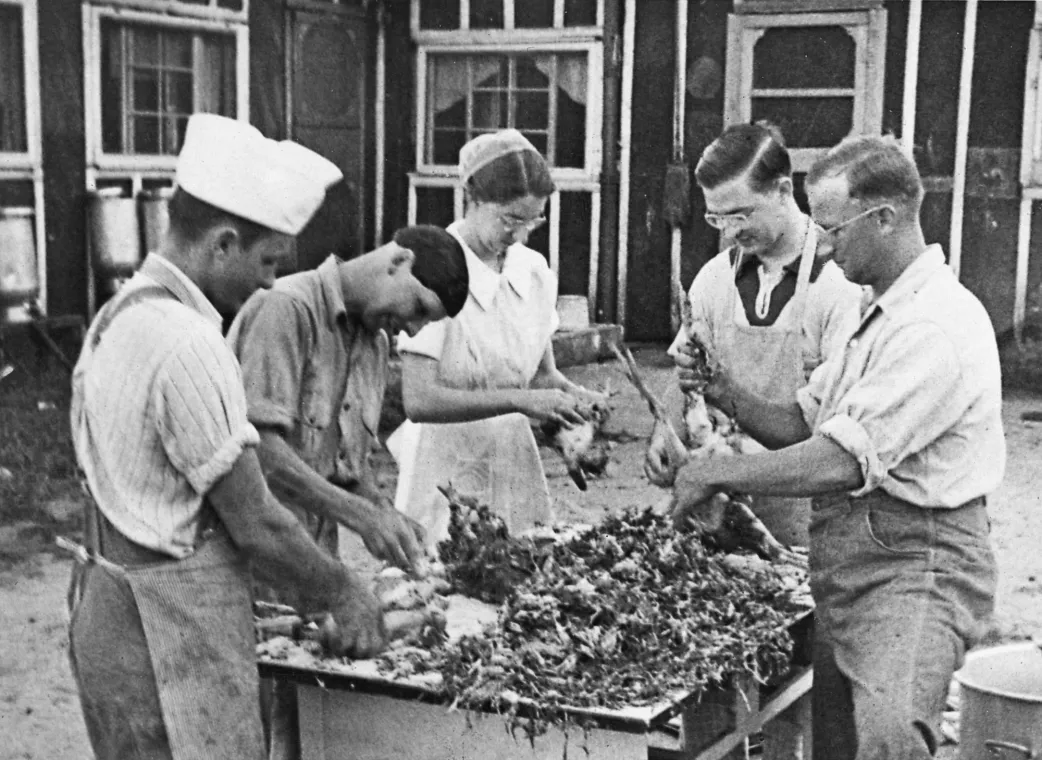 Five people dress chickens outside a kitchen and dining hall.