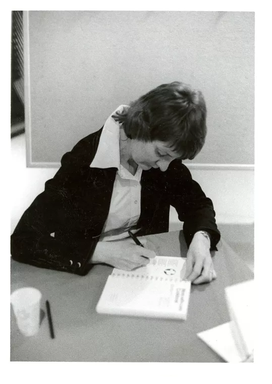 Author sits at a table signing a book.