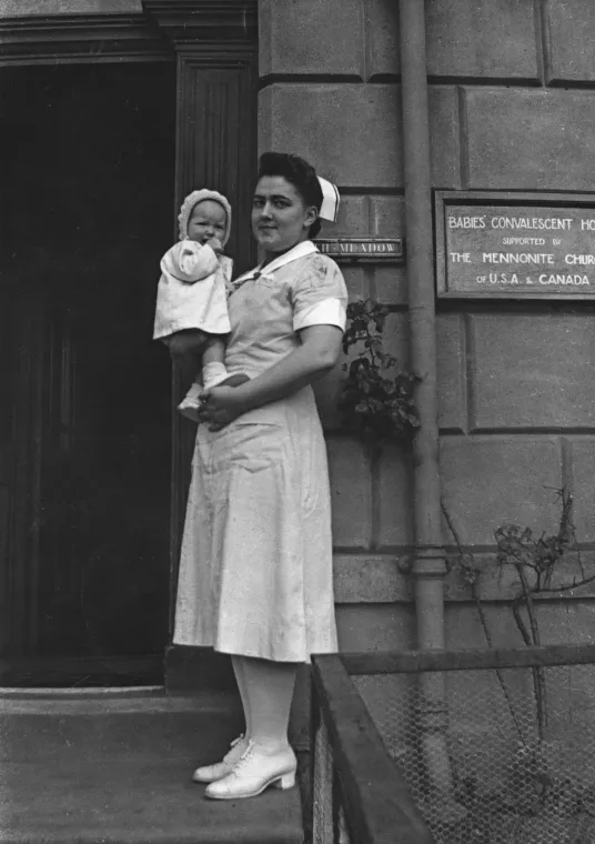 A person stands holding a baby outside of a care home for children.