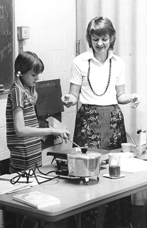 Adult and child stand over an electric skillet during a seminar.