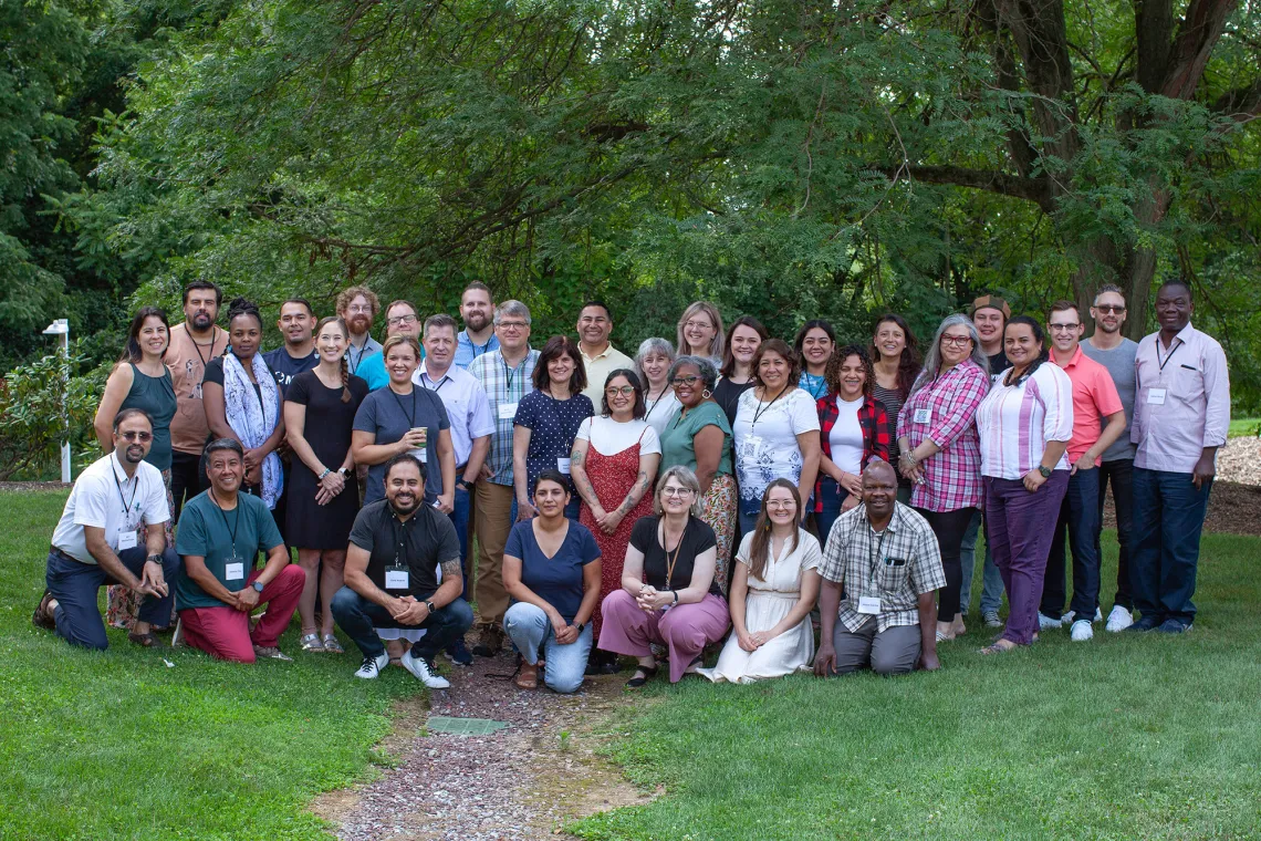 A large group of about 35 people standing under a tree smiling.