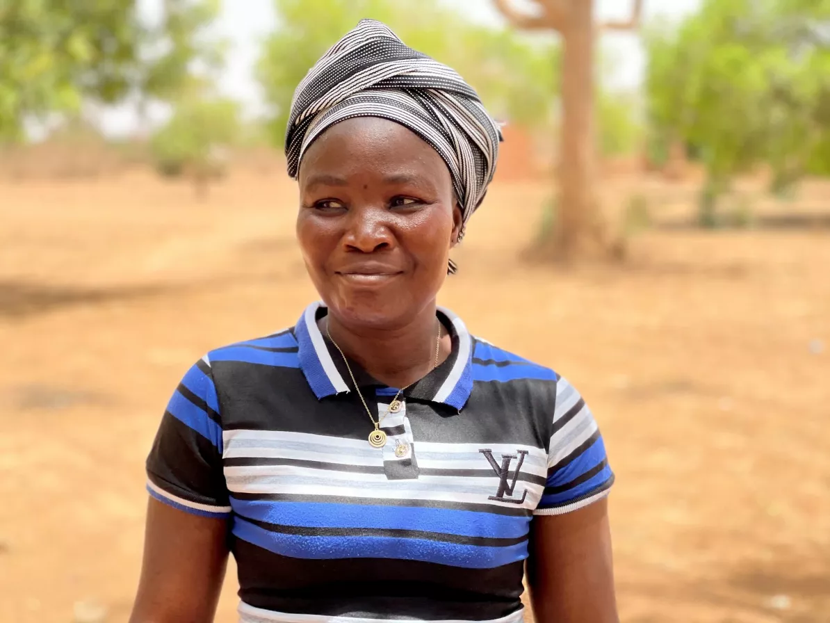 A woman in a blue striped shirt and a hair turban smiles and looks off to the left