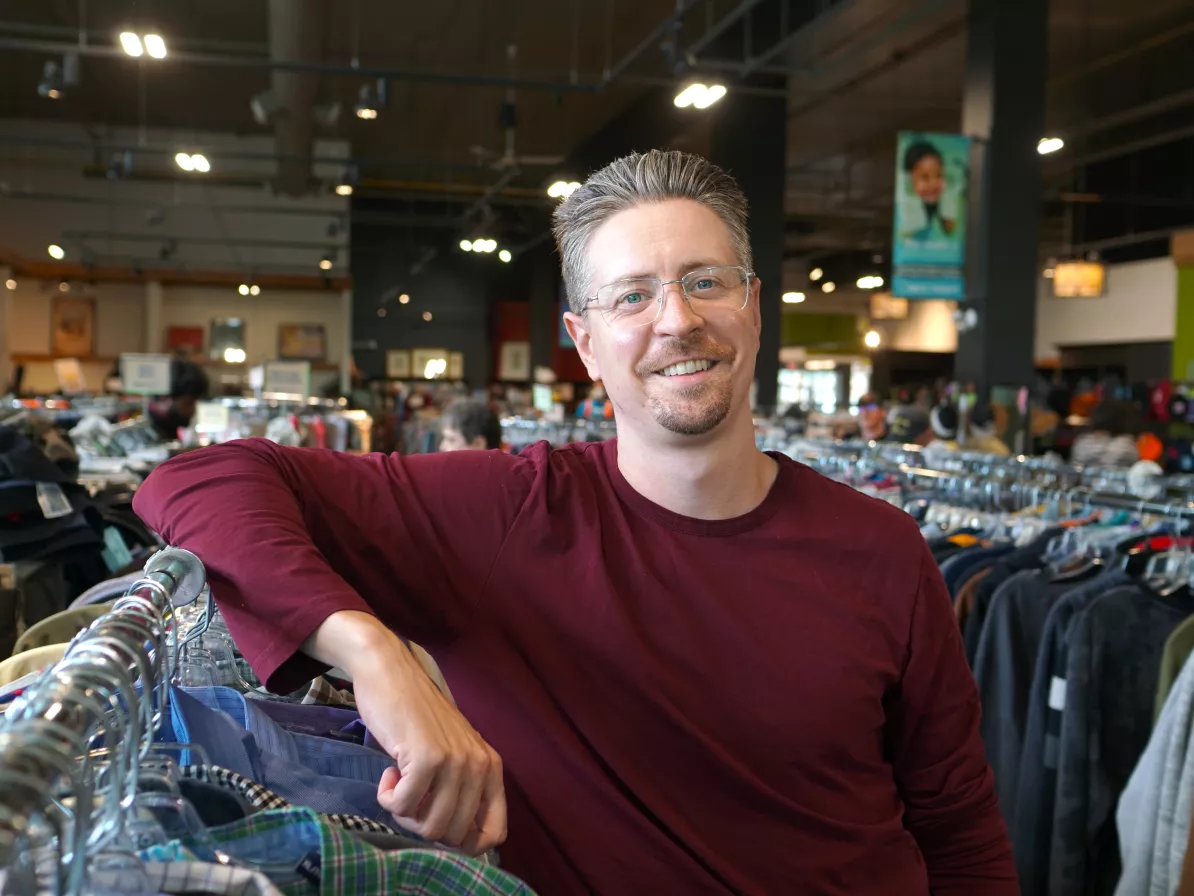 Smiling man leaning on clothing rack