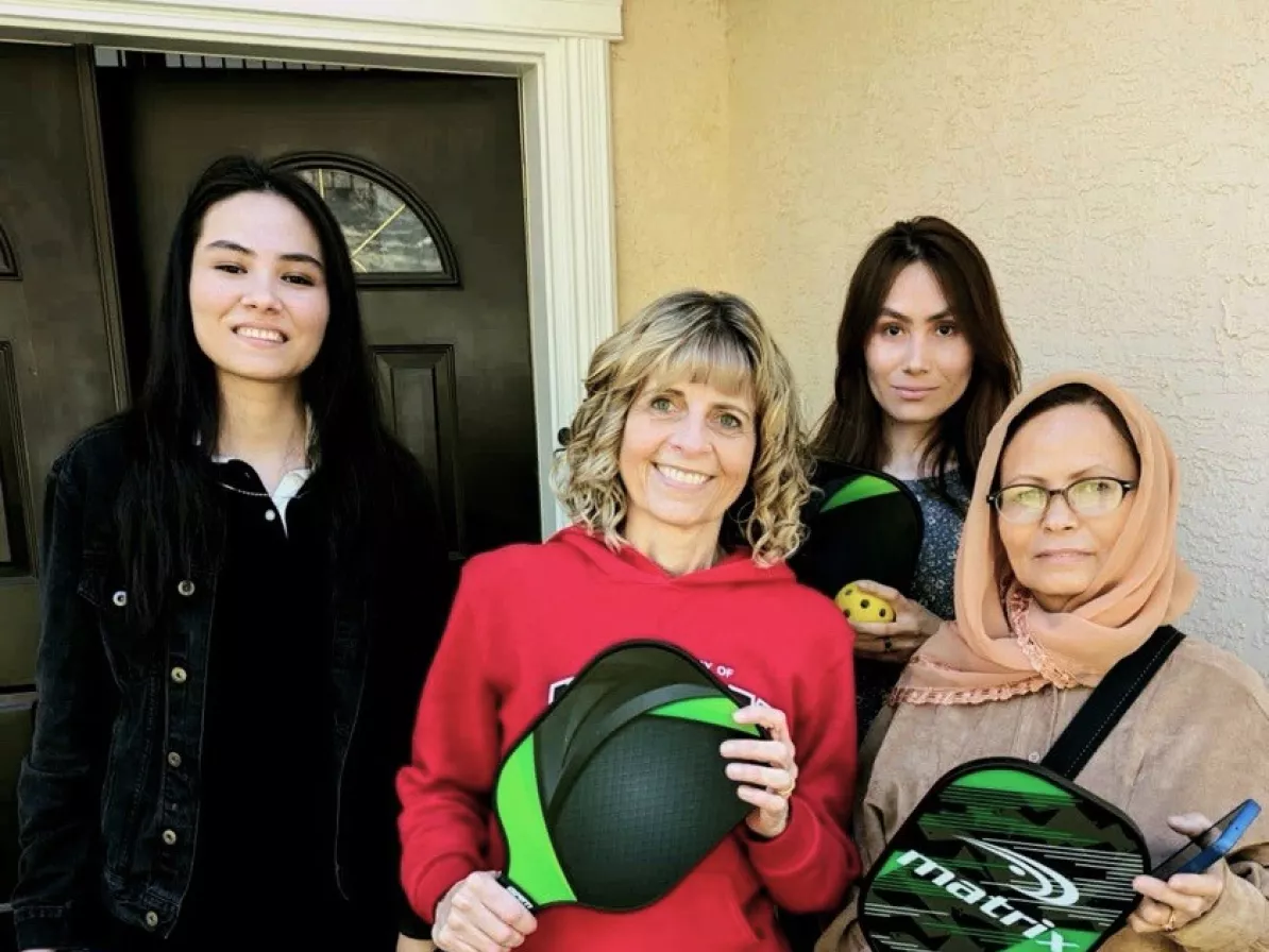 A group of four women, two holding pickleball paddles.