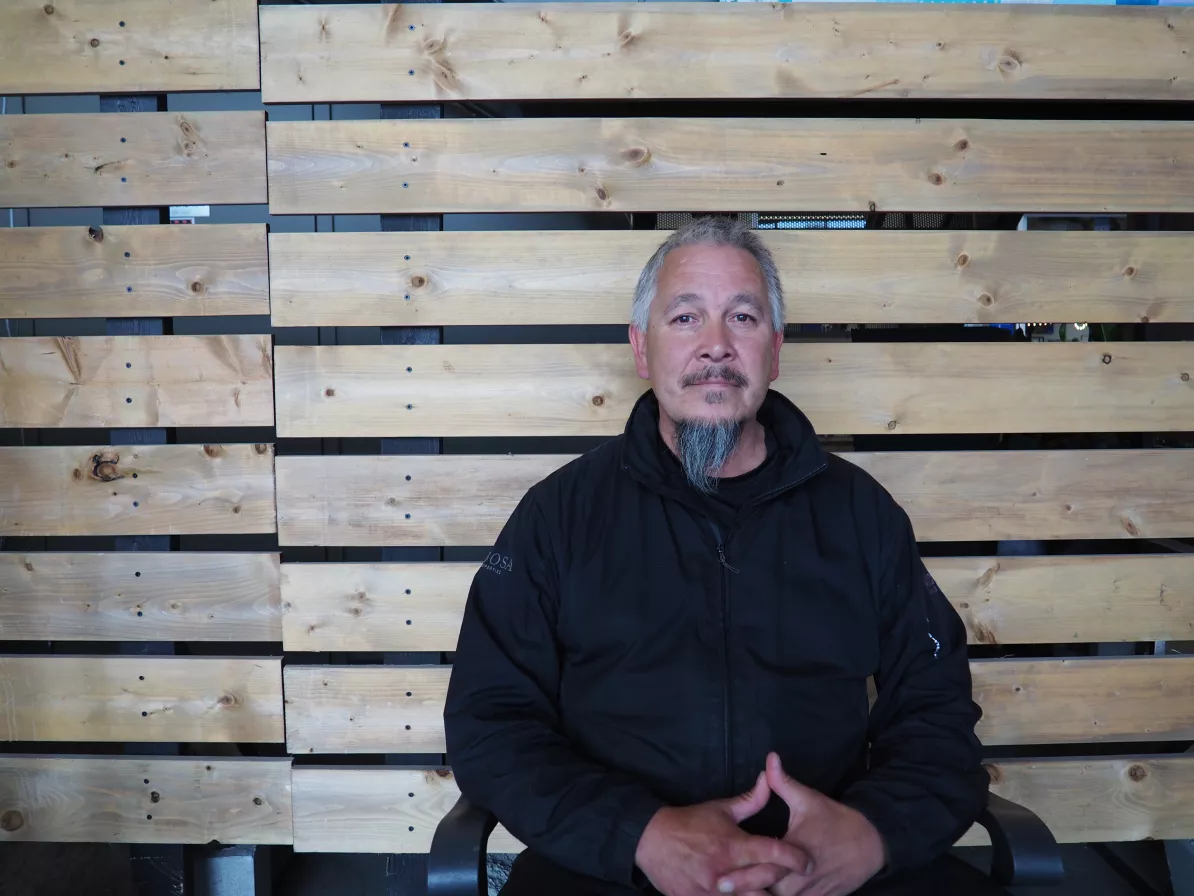 A man seated in front of a wooden slat wall