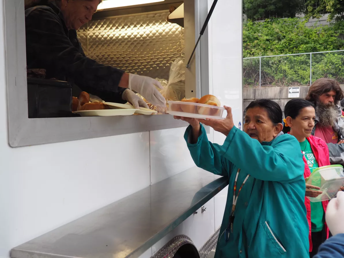 A woman holding a reusable container as it's filled with food by a person in a food trailer