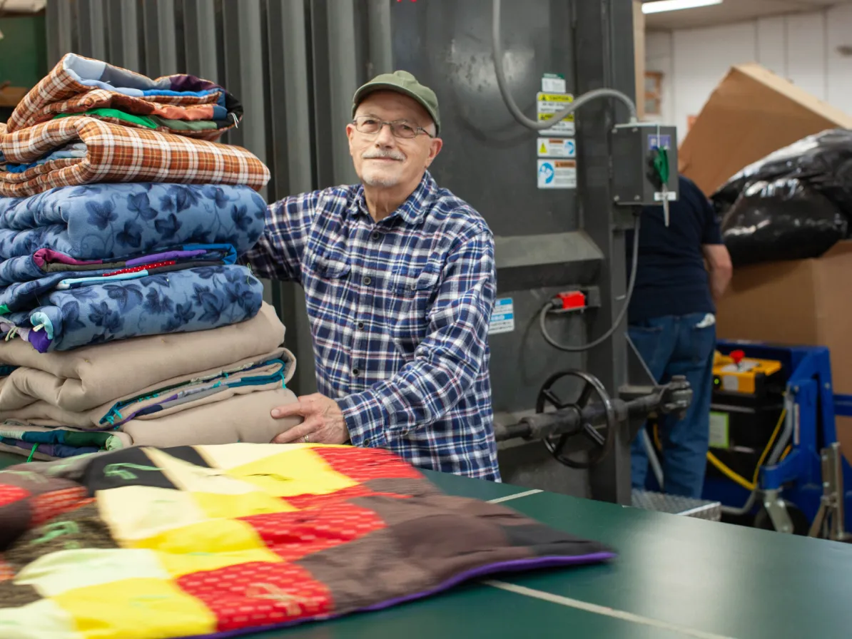 Harold Thomas, a volunteer at the MCC East Coast Material Resources Center, Ephrata, Pennsylvania, helps fold handmade comforters carefully so they can be packaged for shipping. Thomas is from East Pe